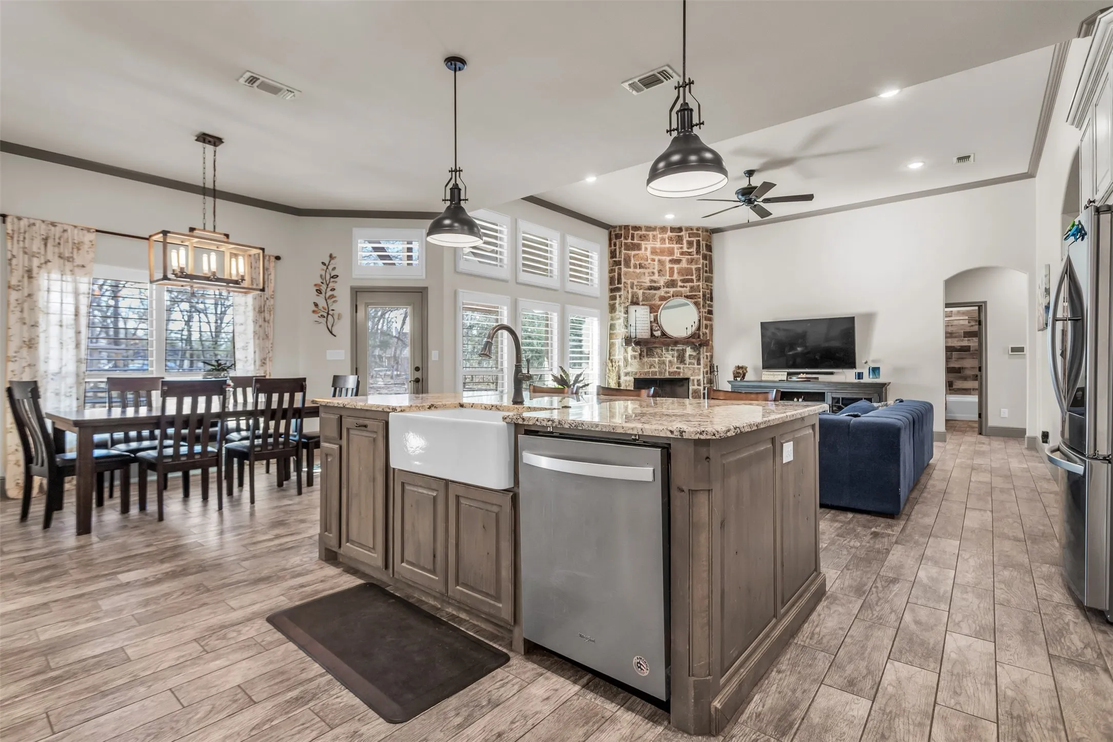 Kitchen featuring arched walkways, light stone countertops, ornamental molding, an island with sink, and stainless steel appliances