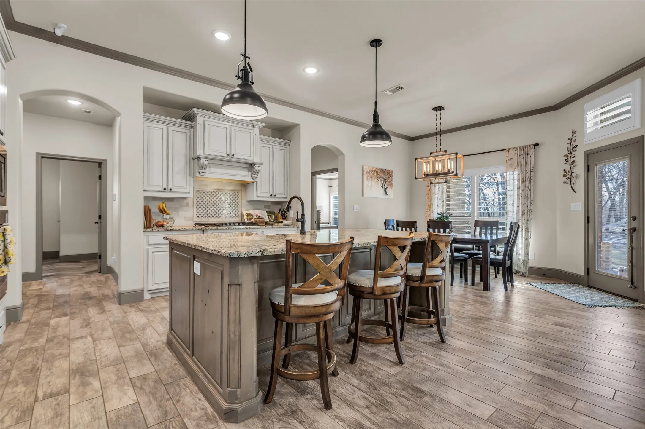Kitchen featuring arched walkways, light stone counters, ornamental molding, pendant lighting, and a center island with sink