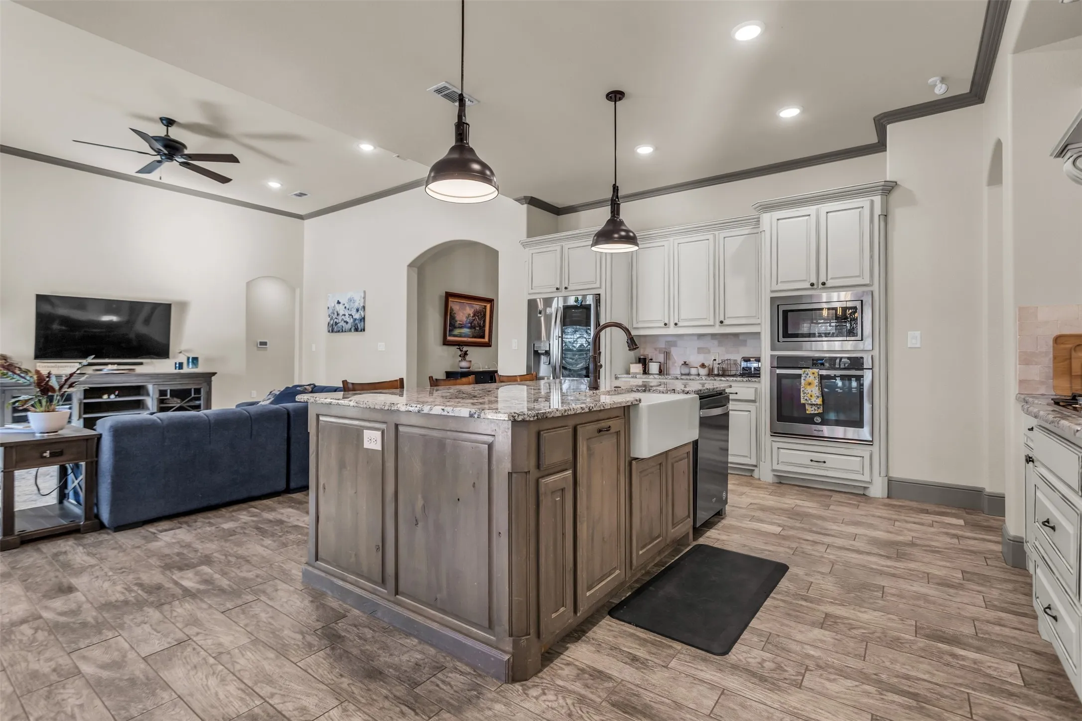 Kitchen featuring arched walkways, decorative backsplash, ornamental molding, hanging light fixtures, and light stone countertops