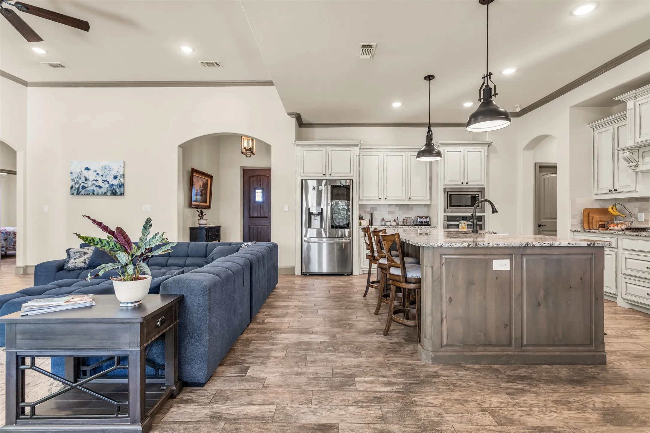 Kitchen featuring arched walkways, crown molding, a center island with sink, appliances with stainless steel finishes, and light stone counters