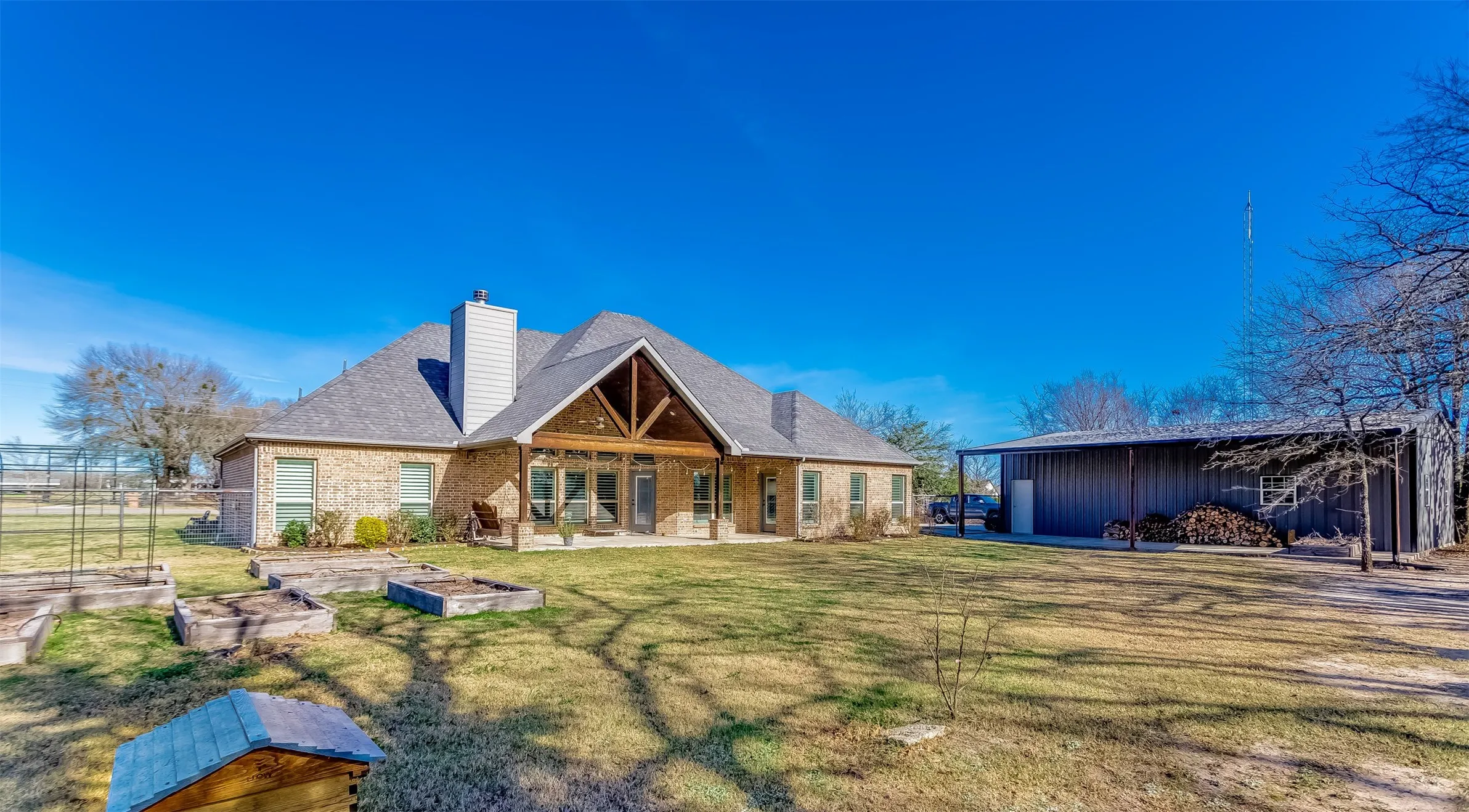 Back of property featuring a patio, a chimney, a vegetable garden, brick siding, and an outdoor structure