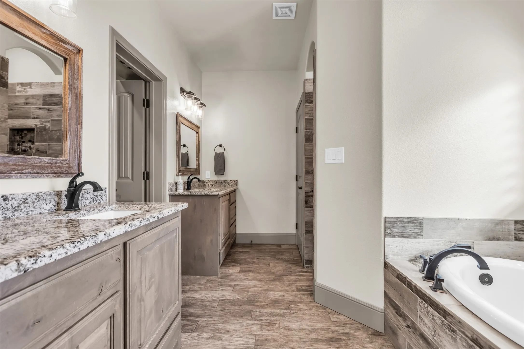 Full bath with two vanities, a garden tub, and light wood finished floors