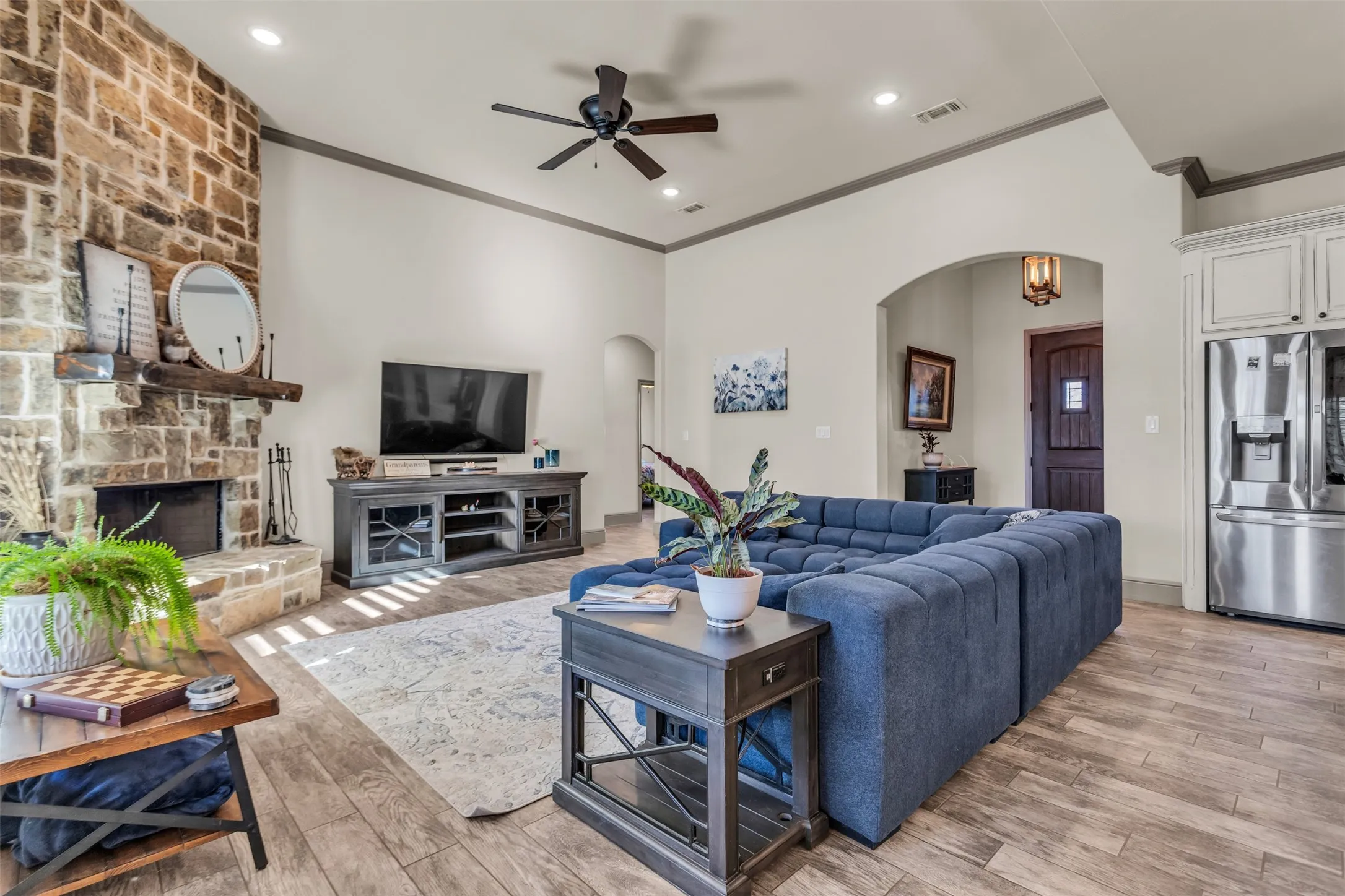 Living area with crown molding, a stone fireplace, arched walkways, light wood-style flooring, and recessed lighting