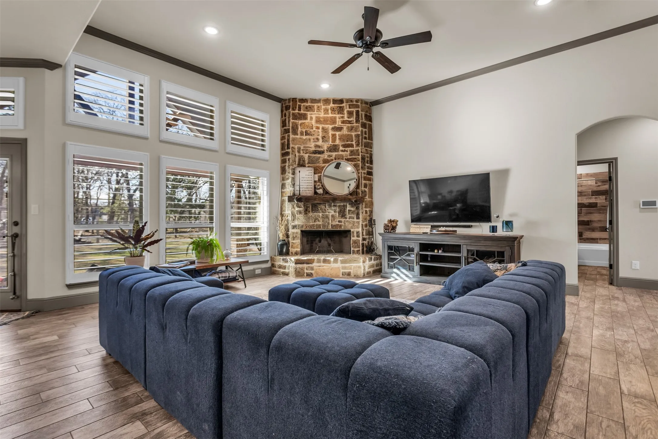 Living room with crown molding, wood finished floors, a fireplace, arched walkways, and a ceiling fan