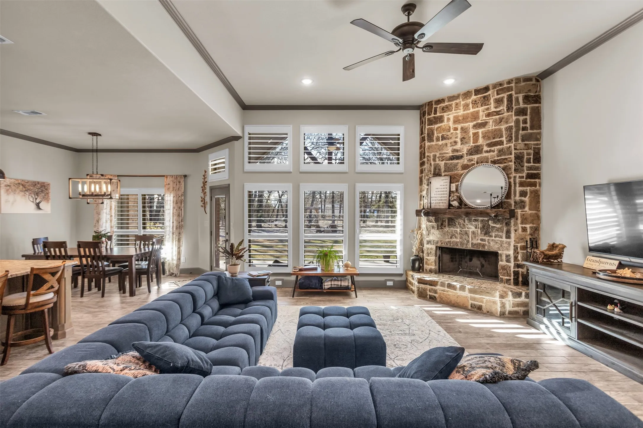 Living room with crown molding, healthy amount of natural light, a stone fireplace, wood finished floors, and ceiling fan