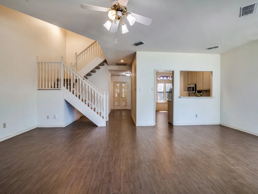 Unfurnished living room featuring ceiling fan, dark wood-style floors, and stairs