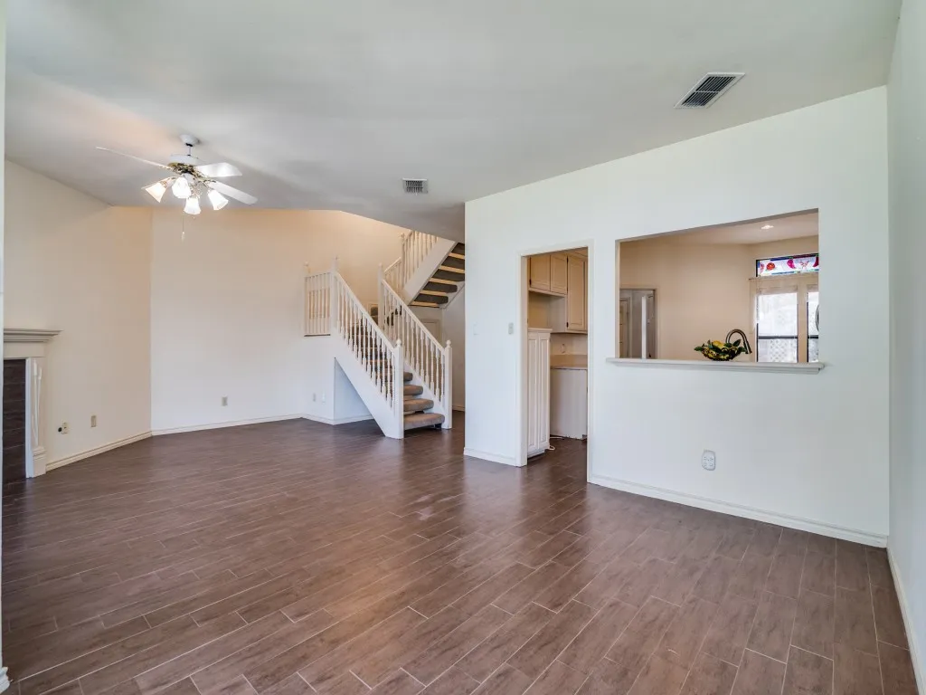 Unfurnished living room with stairs, a ceiling fan, and dark wood-style floors