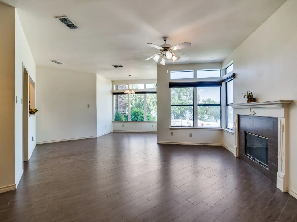 Unfurnished living room featuring ceiling fan, a fireplace, dark wood-style floors, and a chandelier