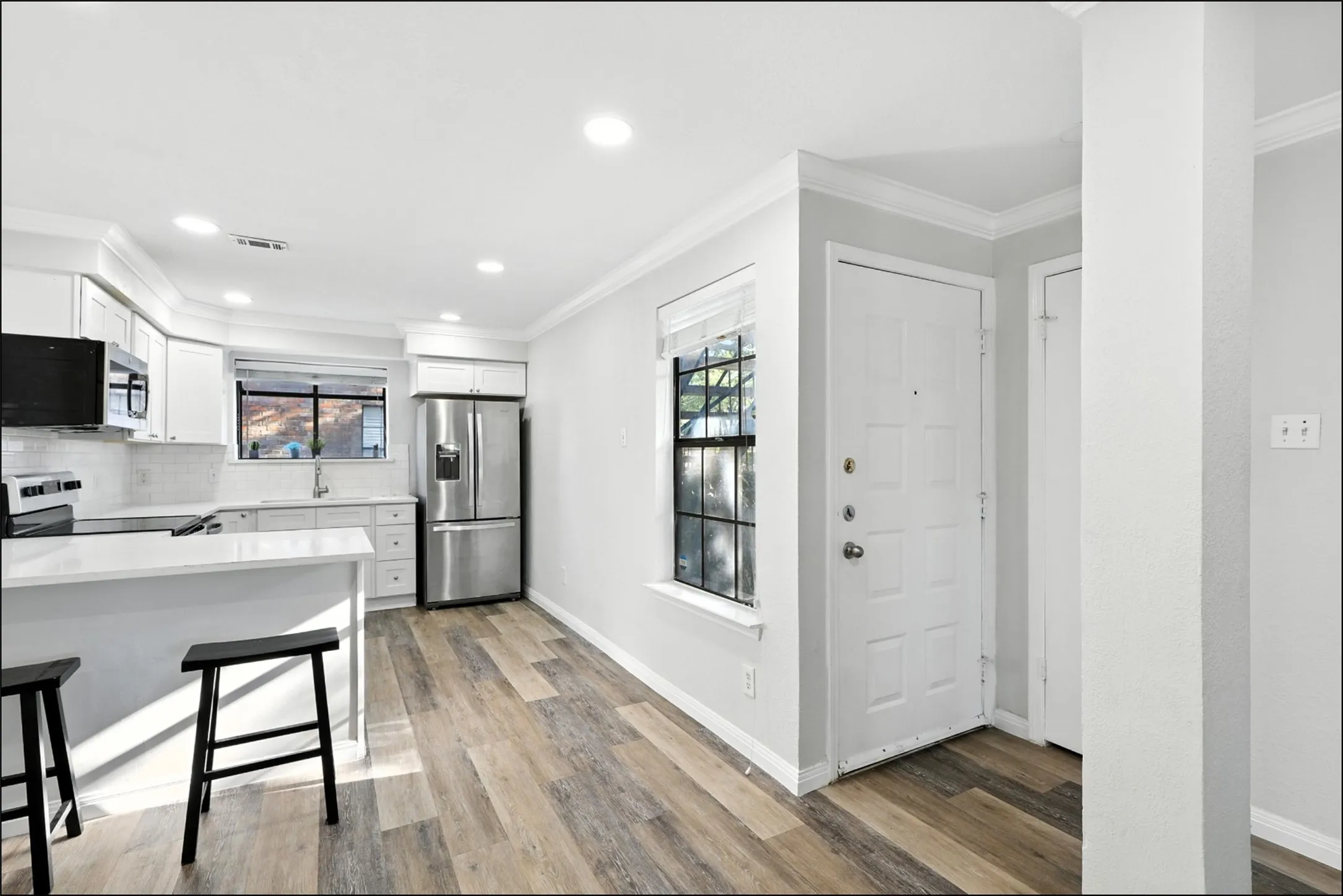 Kitchen with plenty of natural light, white cabinetry, appliances with stainless steel finishes, ornamental molding, and a breakfast bar
