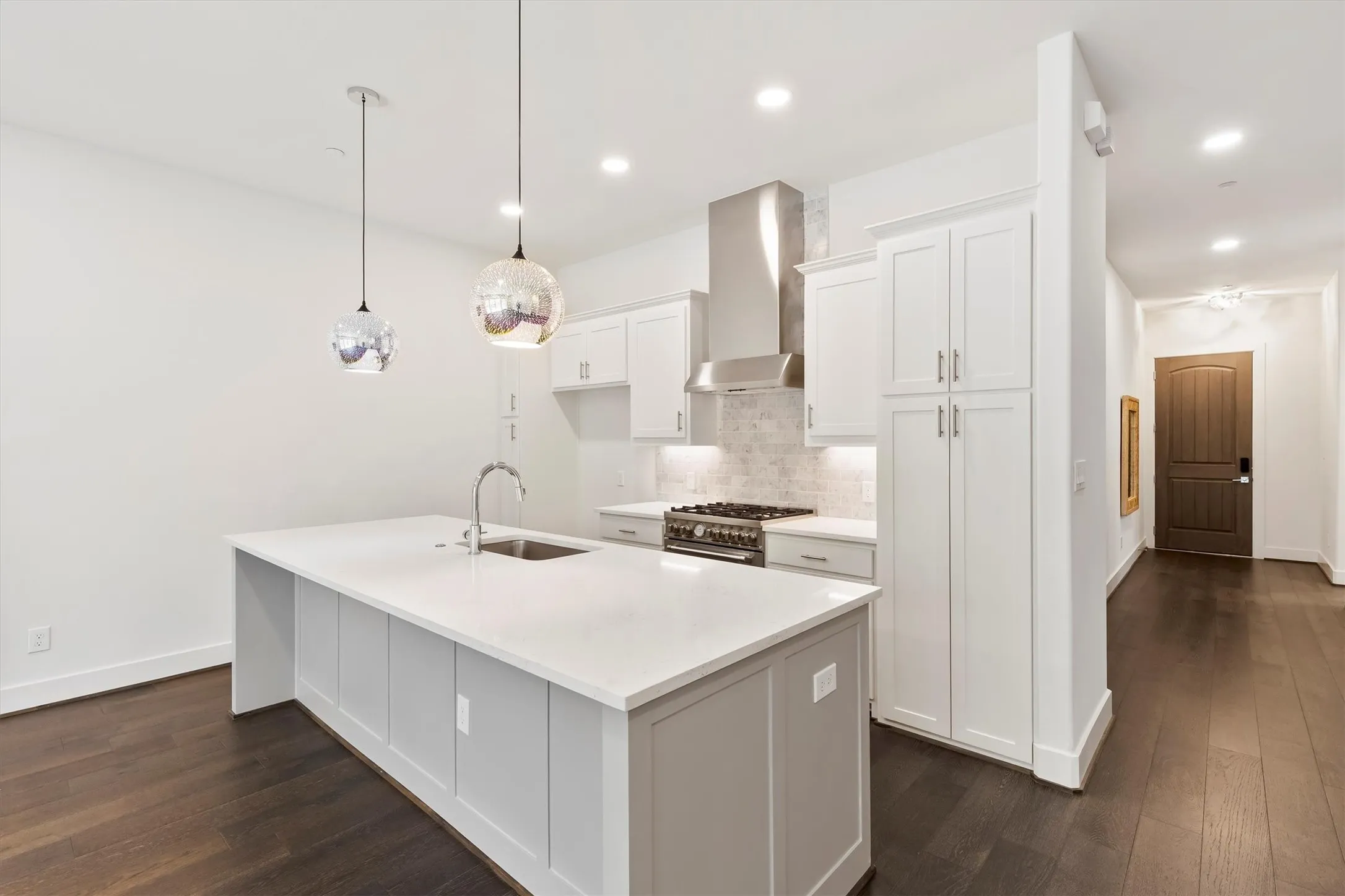 Kitchen featuring decorative backsplash, a center island with sink, wall chimney exhaust hood, white cabinets, and hanging light fixtures