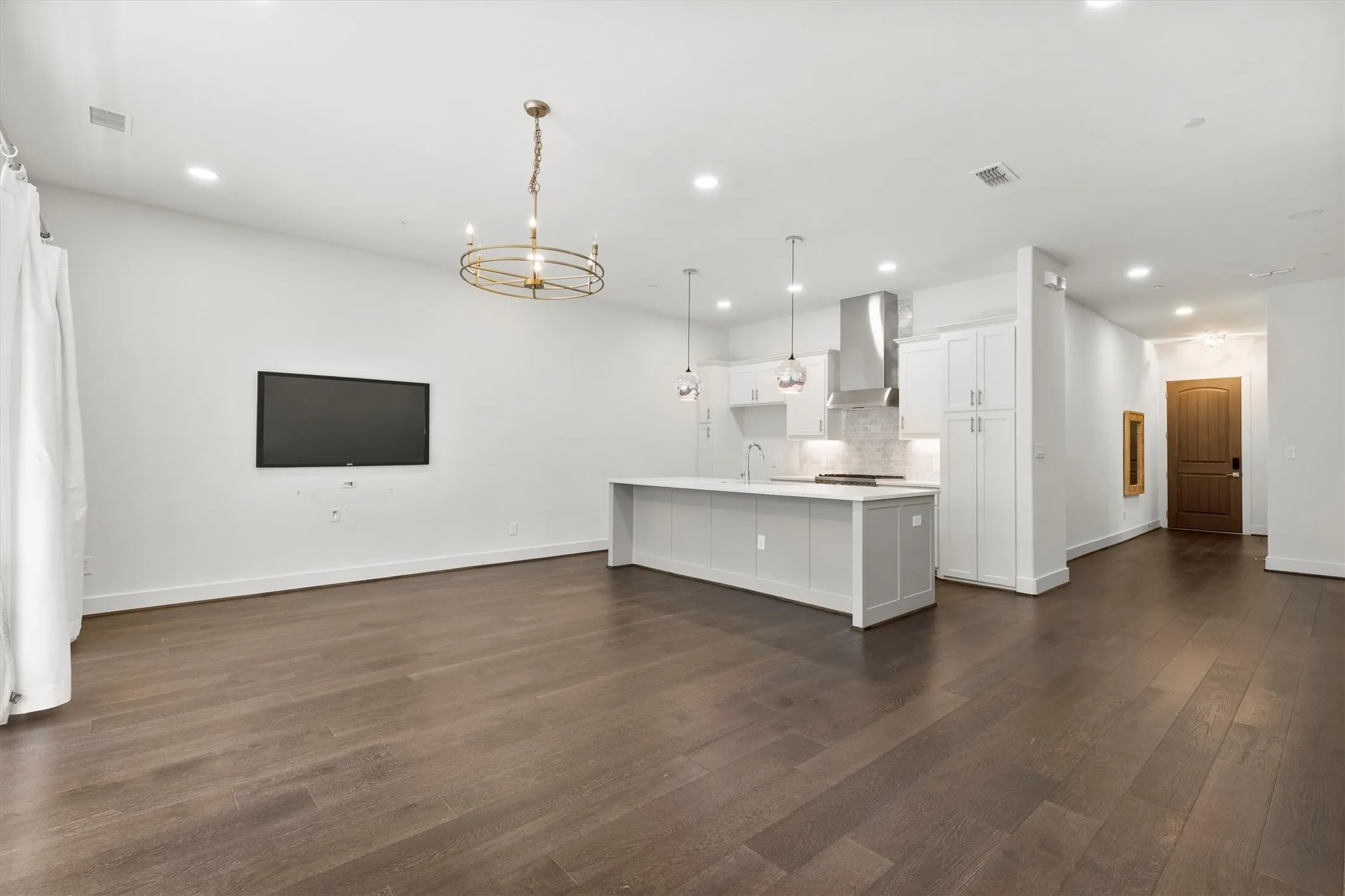 Kitchen with open floor plan, decorative light fixtures, white cabinets, a kitchen island with sink, and dark wood finished floors