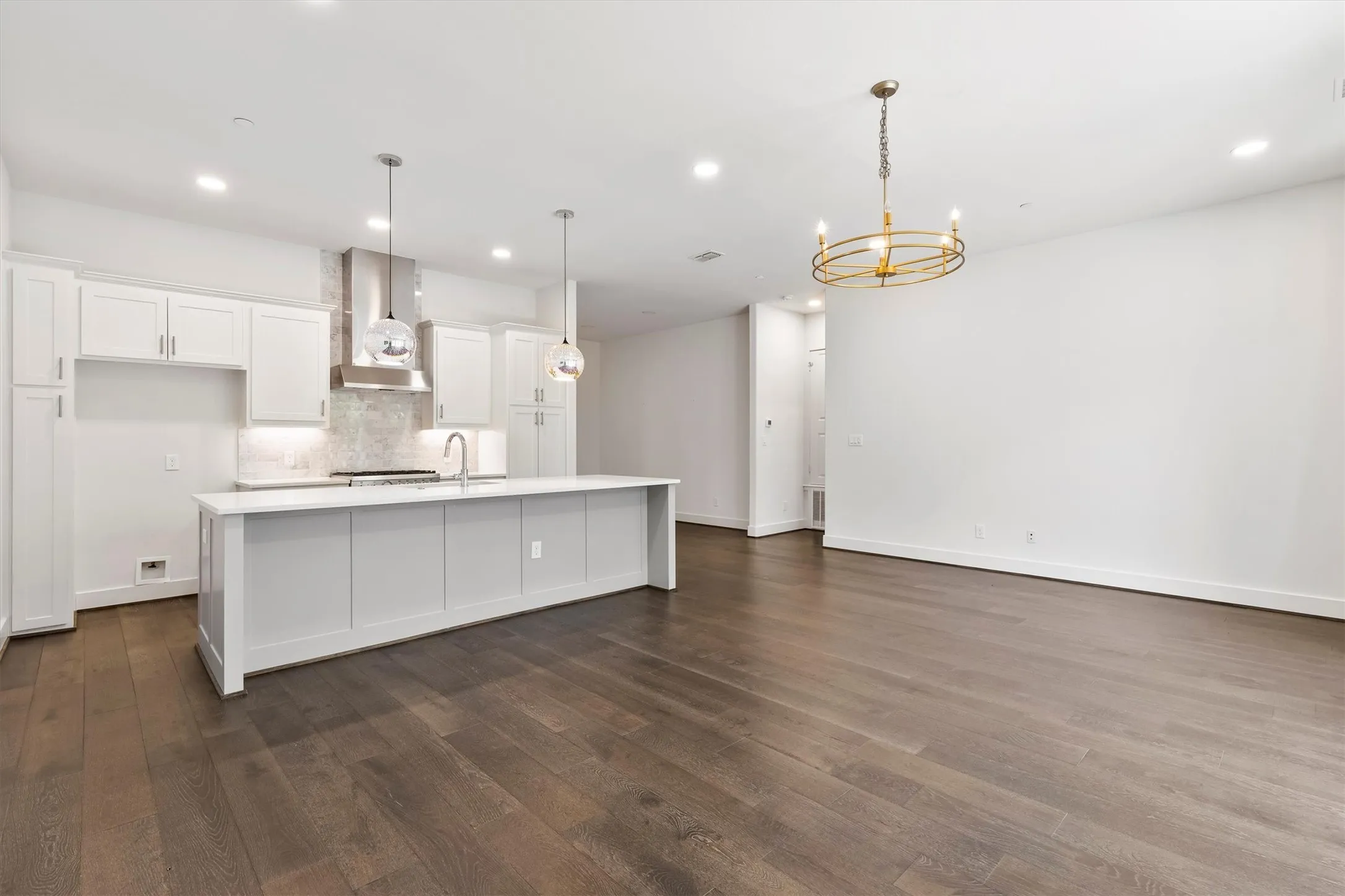 Kitchen with white cabinets, a center island with sink, hanging light fixtures, wall chimney range hood, and a chandelier.