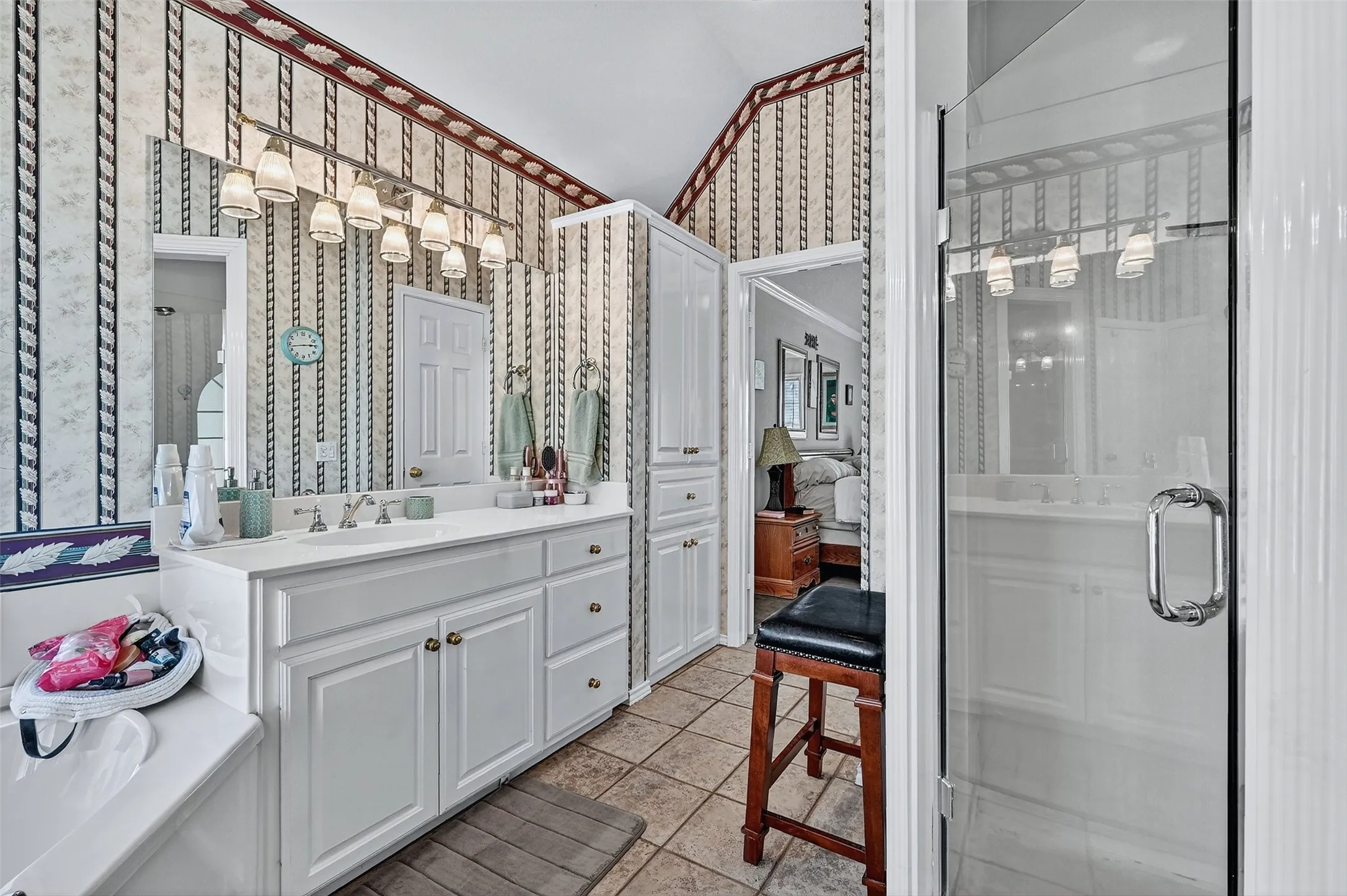 Ensuite bathroom with wallpapered walls, vanity, tile patterned flooring, a stall shower, and a chandelier