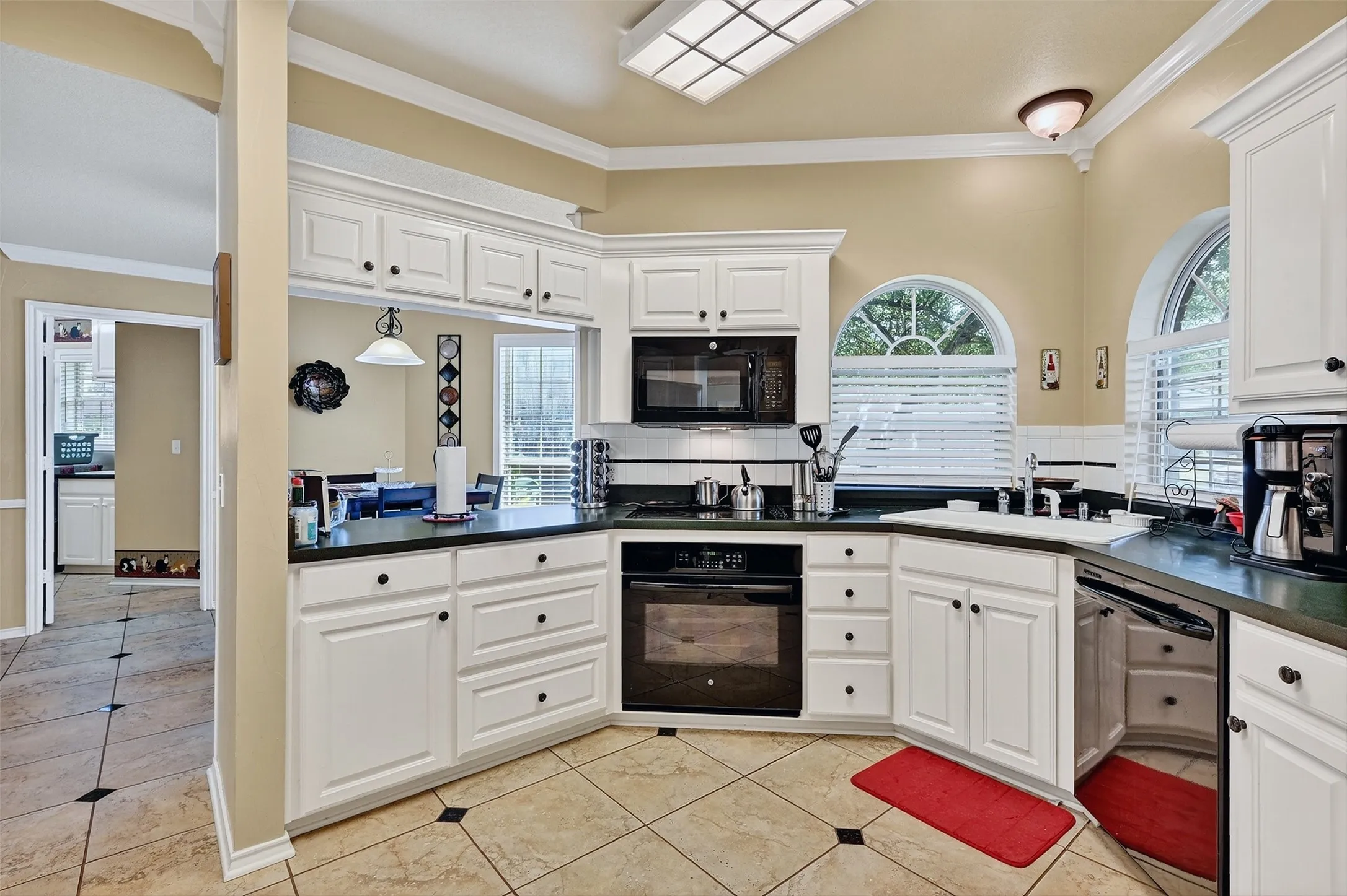 Kitchen with black appliances, dark countertops, light tile patterned flooring, ornamental molding, and decorative backsplash