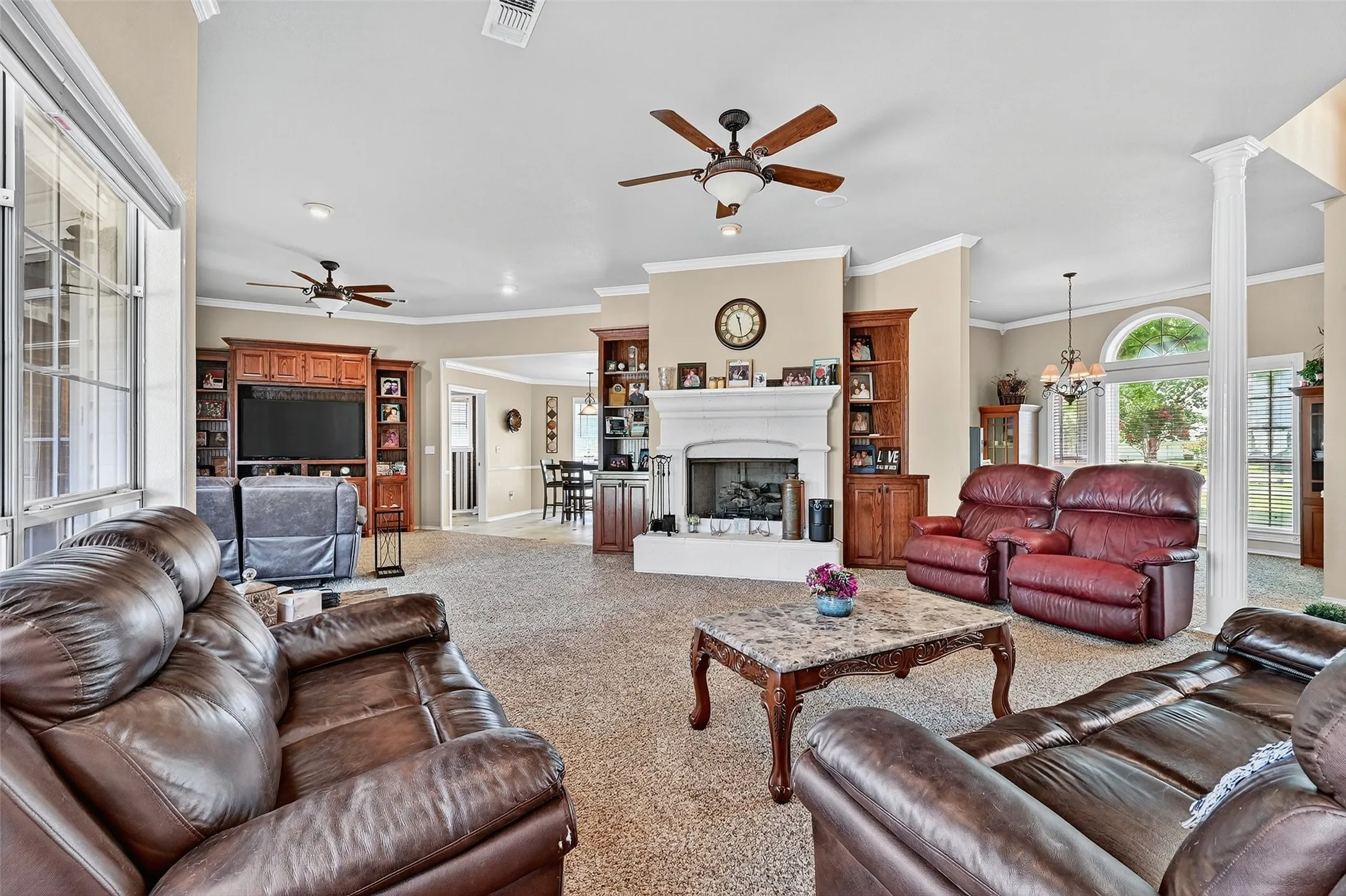 Living area with a ceiling fan, ornamental molding, carpet floors, a fireplace with raised hearth, and ornate columns