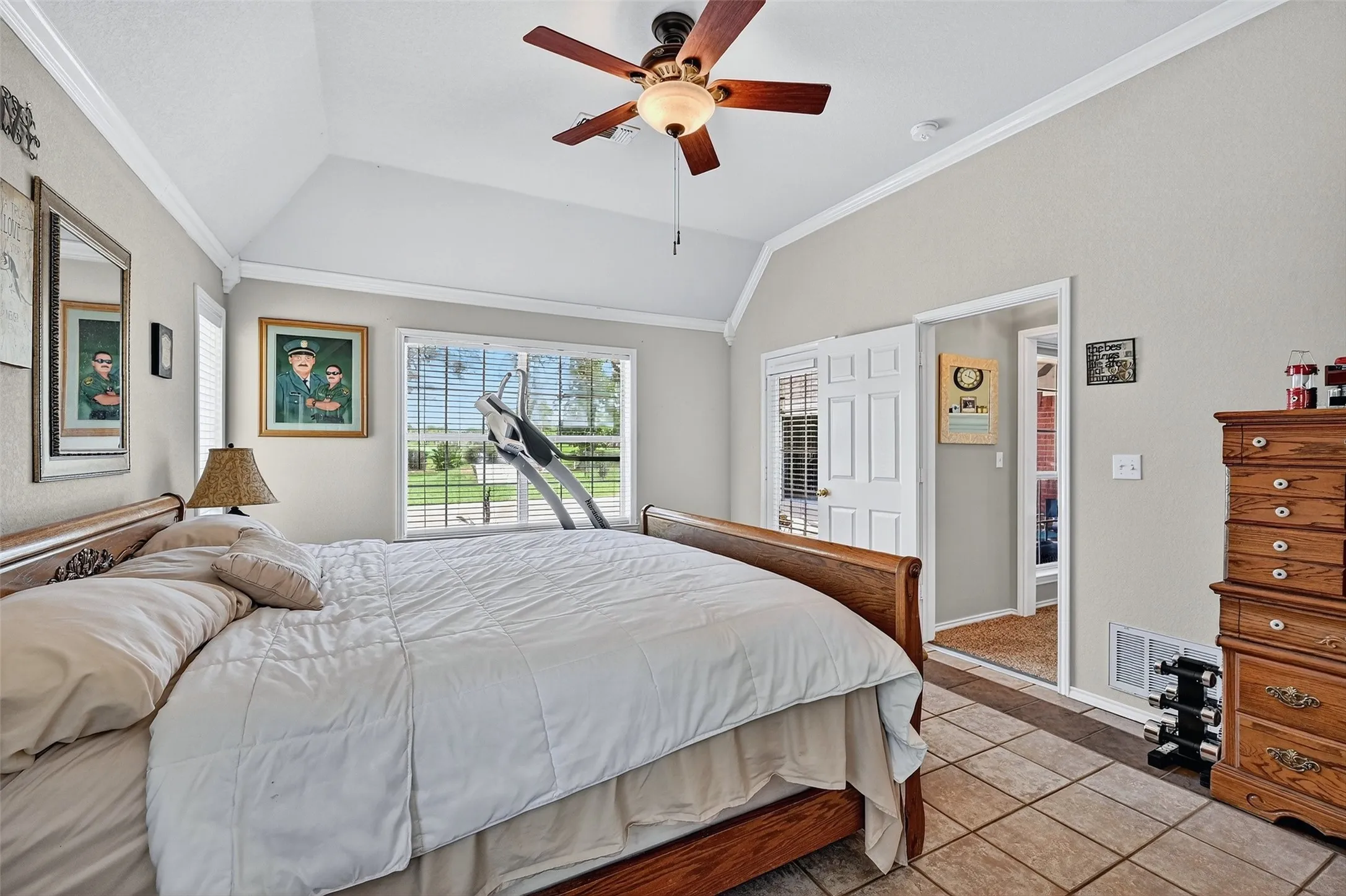 Bedroom featuring lofted ceiling, crown molding, light tile patterned floors, and a ceiling fan