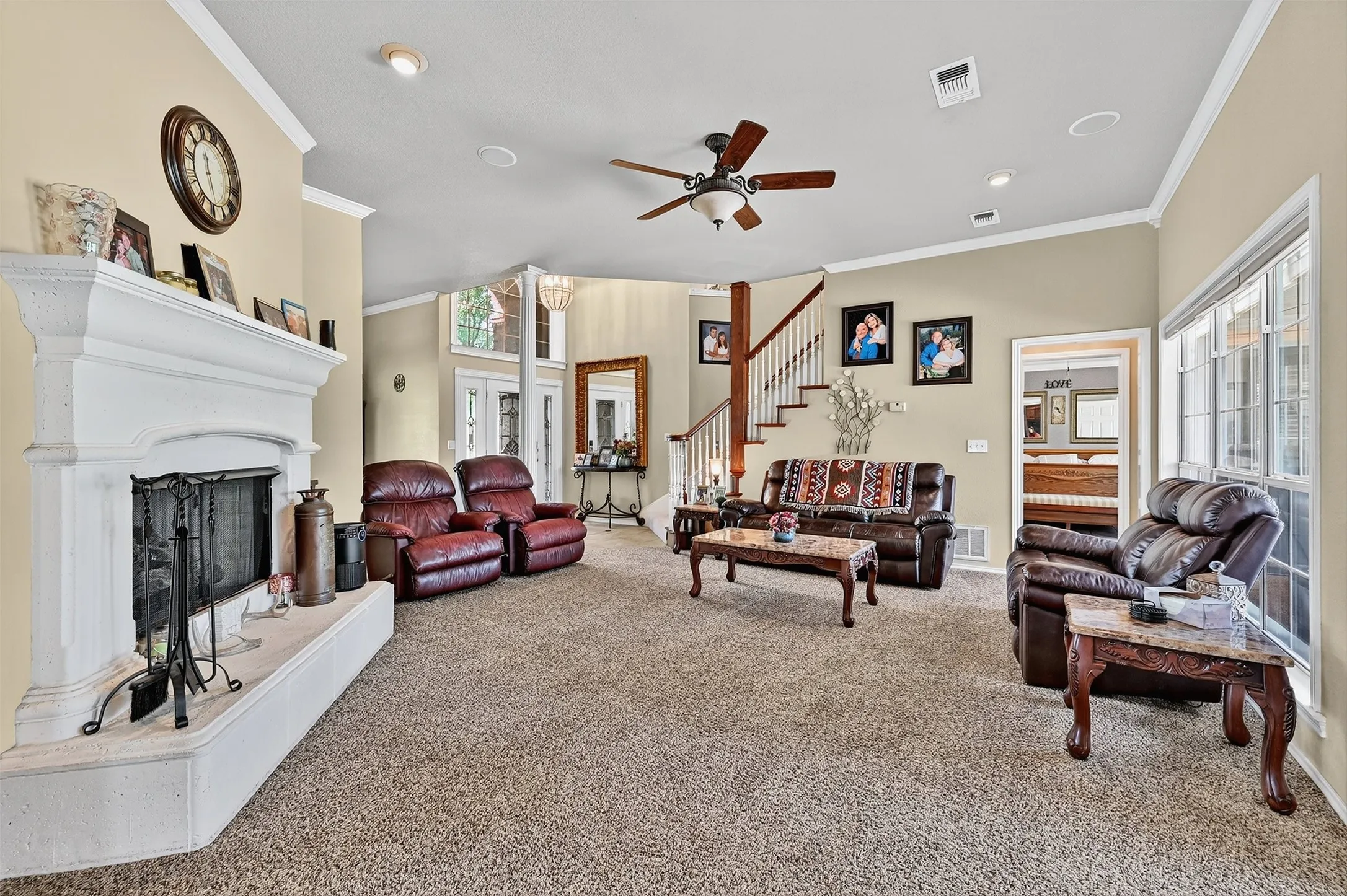 Living room featuring ornamental molding, carpet floors, a ceiling fan, a fireplace with raised hearth, and stairway
