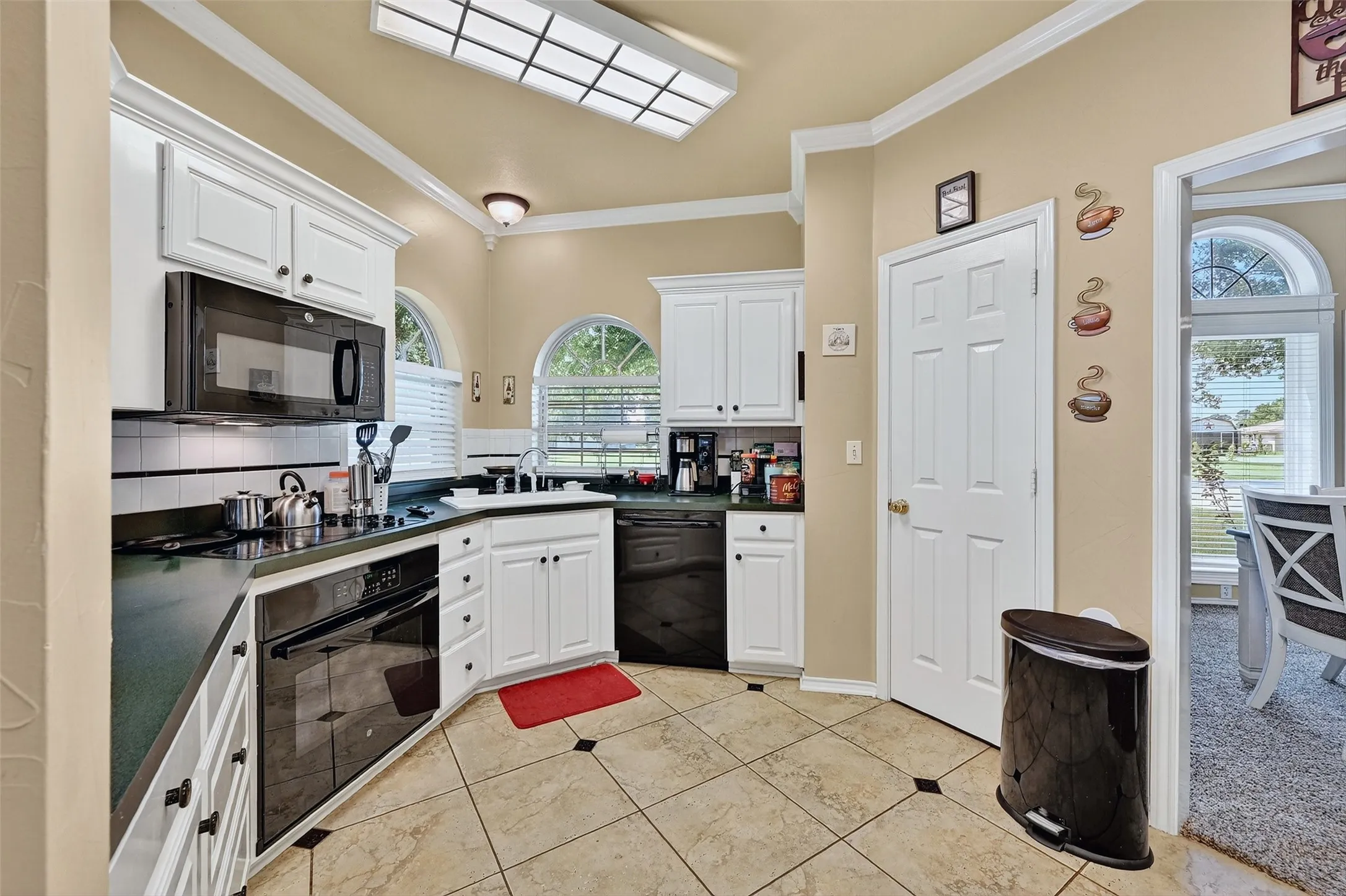 Kitchen featuring crown molding, black appliances, dark countertops, white cabinetry, and tasteful backsplash