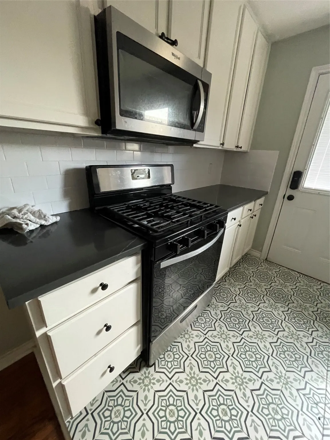Kitchen featuring stainless steel gas stove, dark countertops, backsplash, and white cabinetry