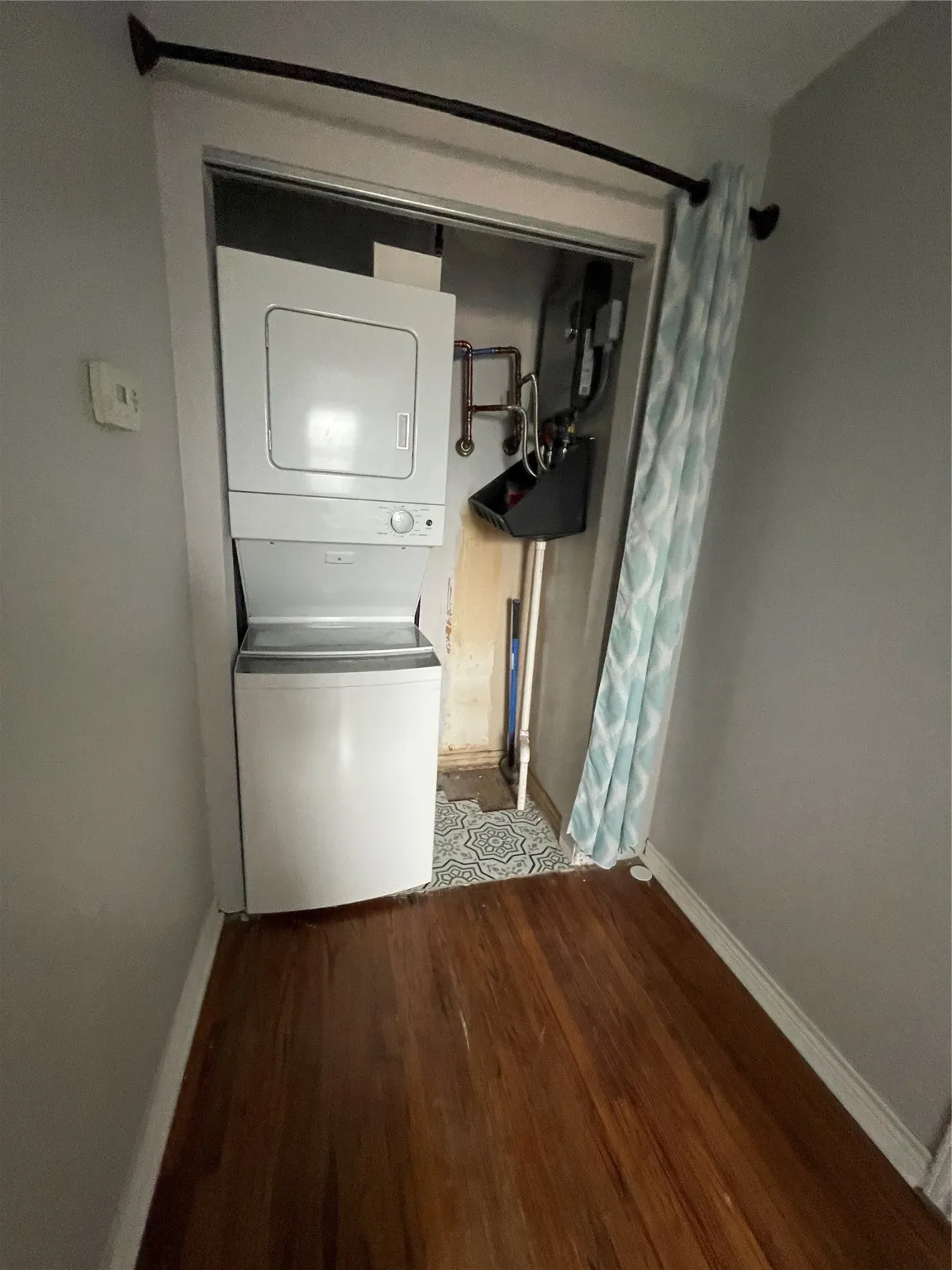 Washroom with stacked washer / drying machine and wood finished floors