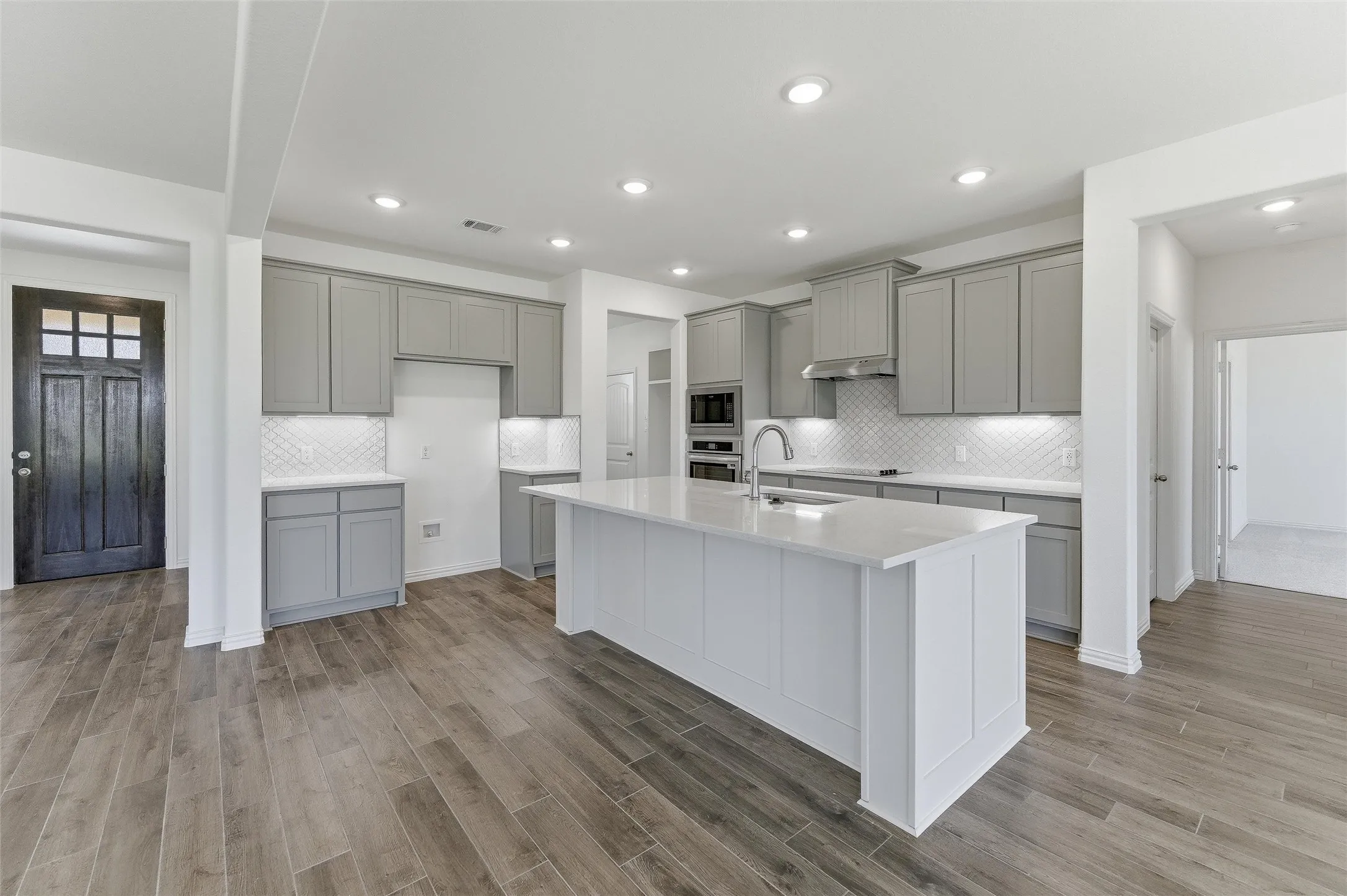 Modern kitchen featuring a large central island with a solid surface countertop, light gray cabinetry, and a white subway tile backsplash