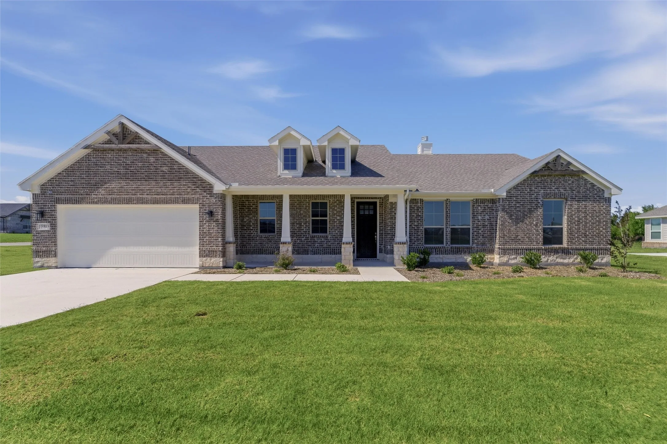 Brick exterior with stone accents, a covered front porch, and a two-car garage