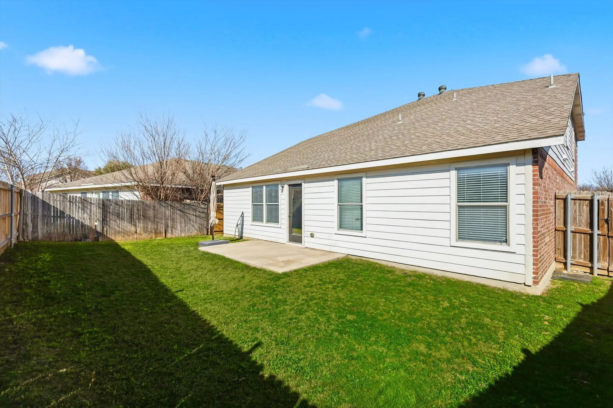 Rear view of property with a patio area, roof with shingles, a fenced backyard, and brick siding