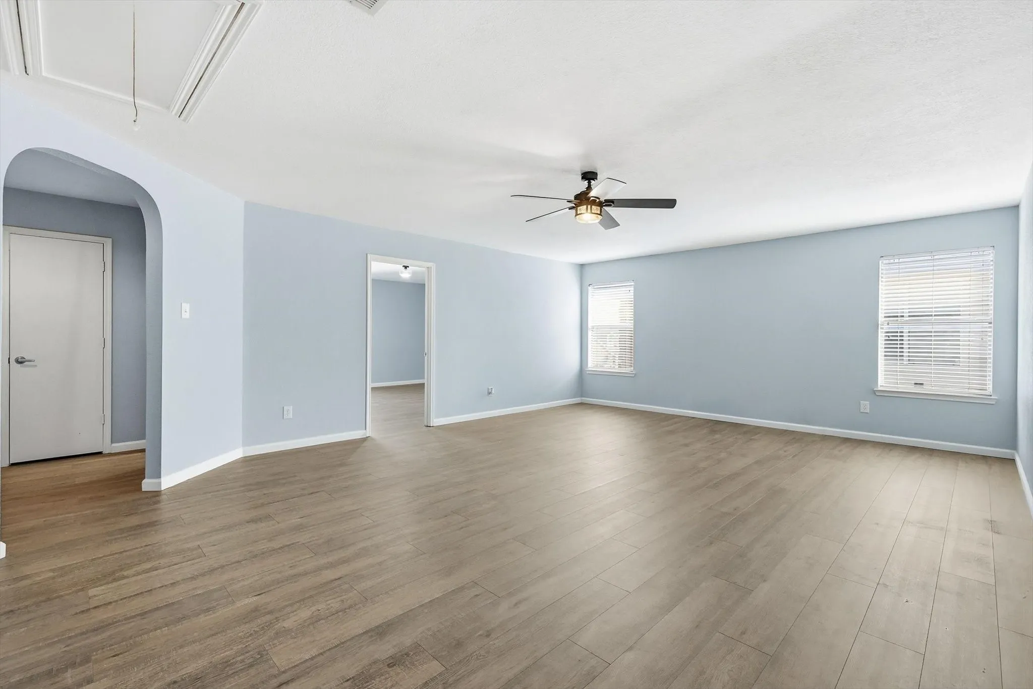 Unfurnished room featuring arched walkways, attic access, wood finished floors, and ceiling fan