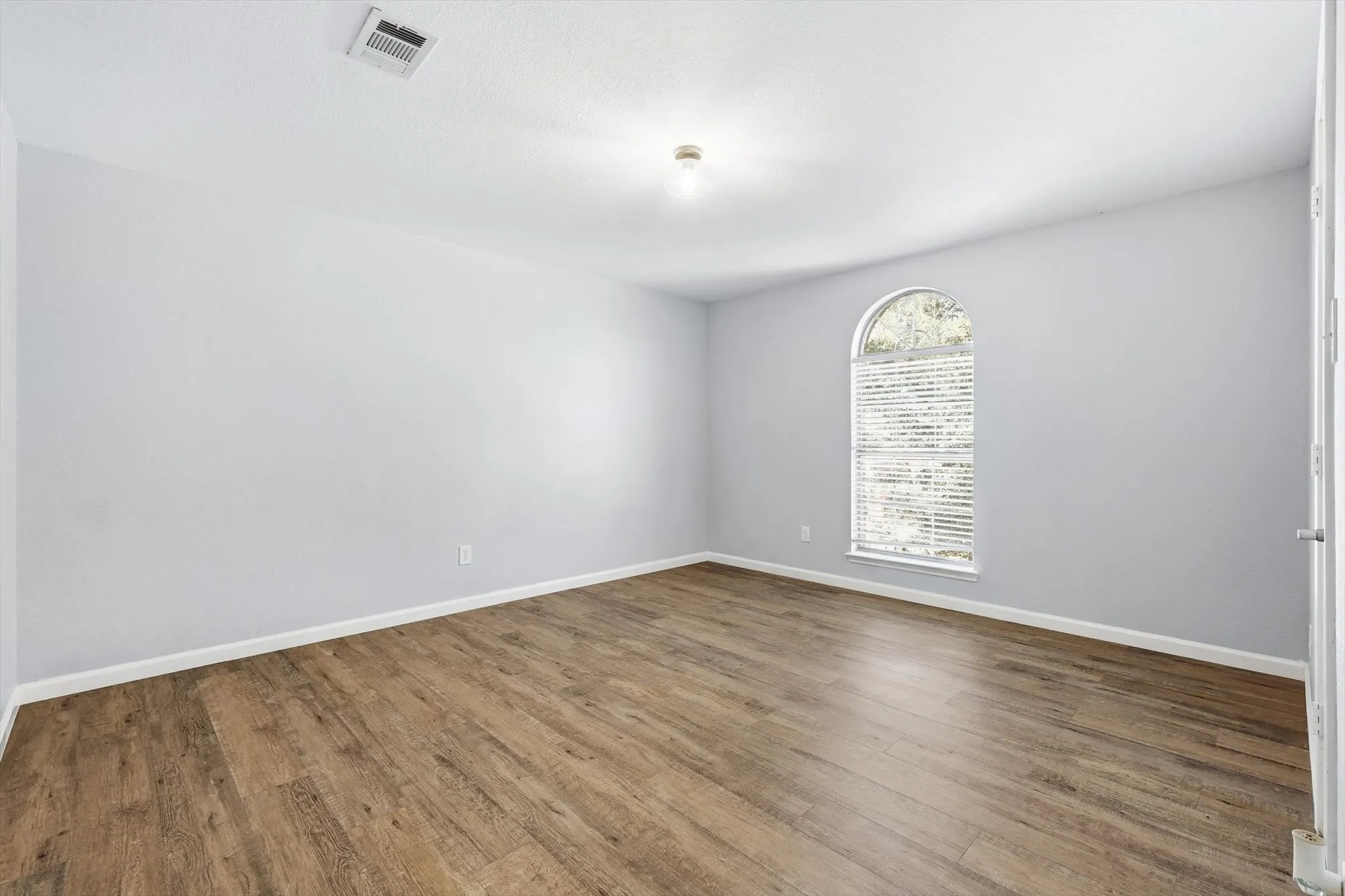 Unfurnished bedroom featuring arched walkways and wood finished floors