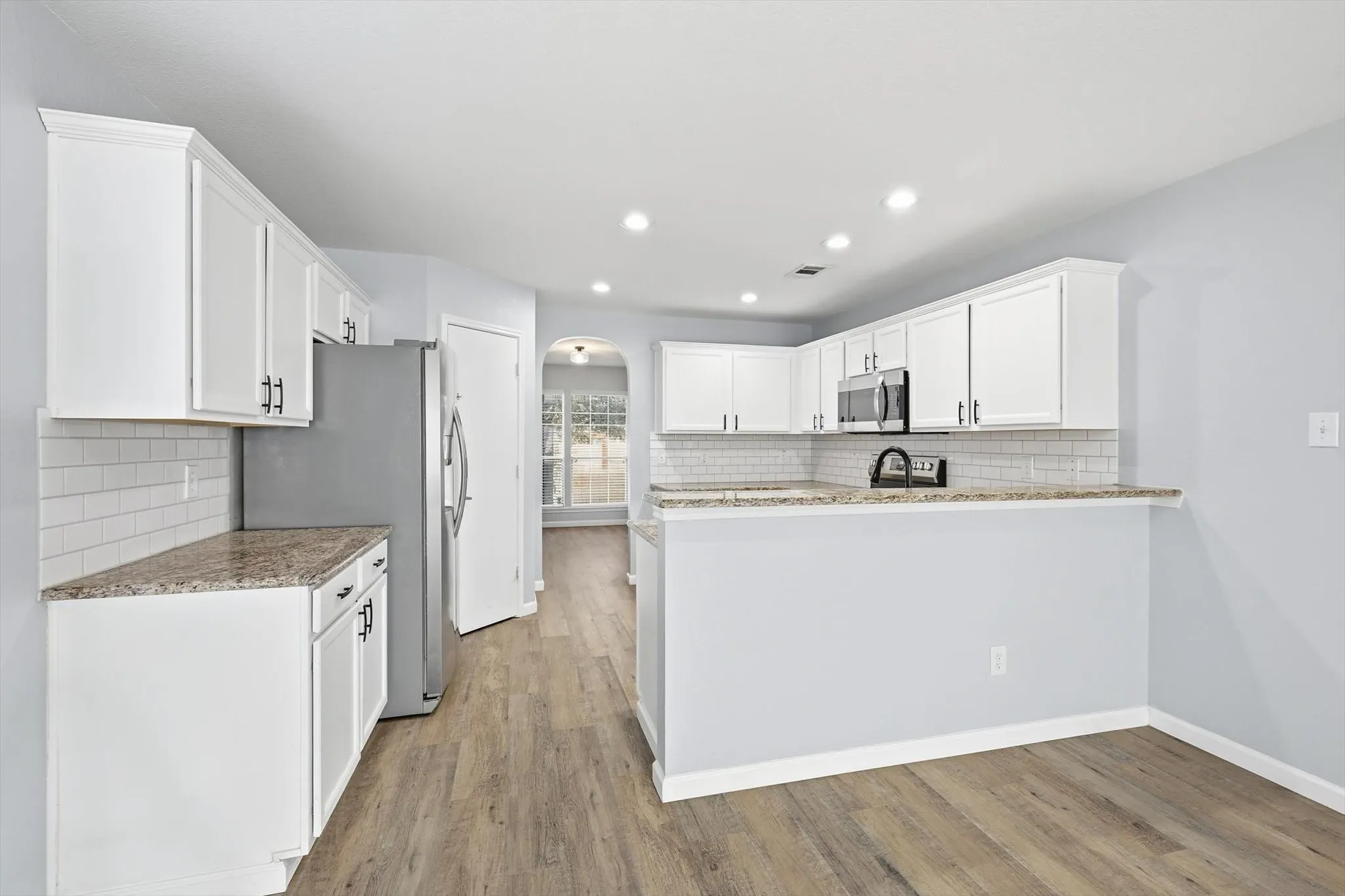 Kitchen with arched walkways, white cabinetry, backsplash, light stone countertops, and recessed lighting