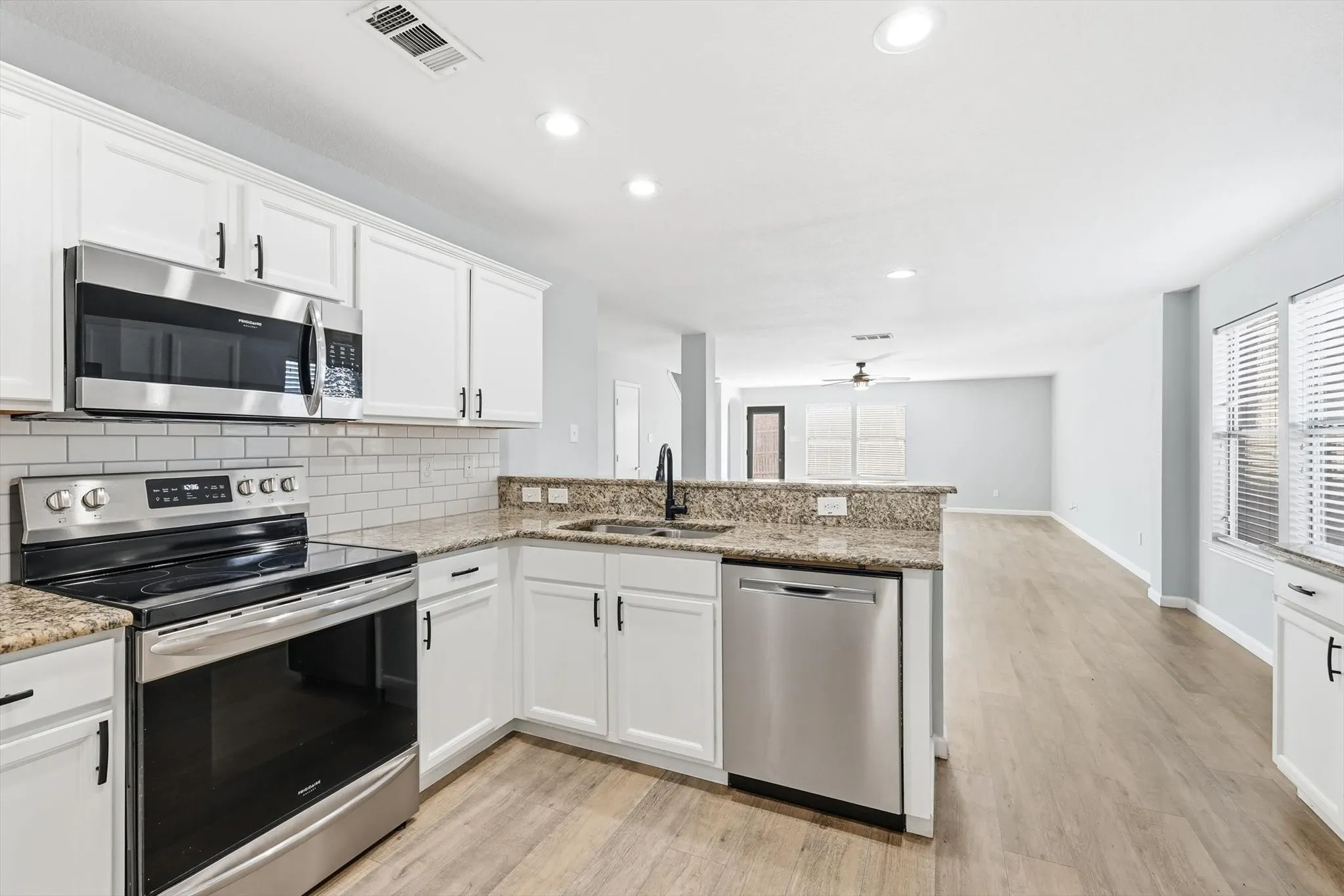Kitchen with arched walkways, white cabinetry, backsplash, light stone countertops, and recessed lighting