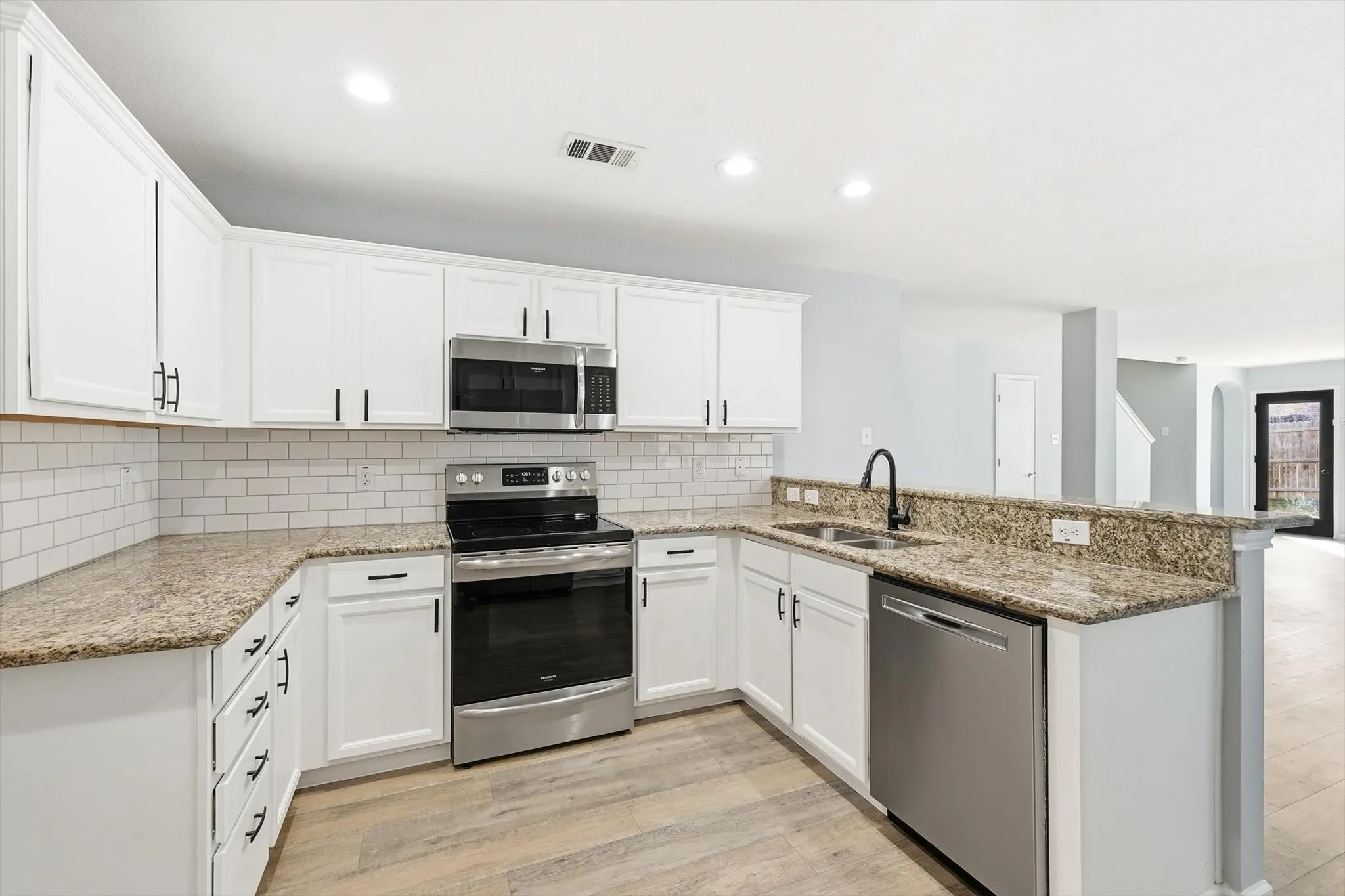 Kitchen featuring appliances with stainless steel finishes, light stone countertops, a peninsula, white cabinetry, and recessed lighting
