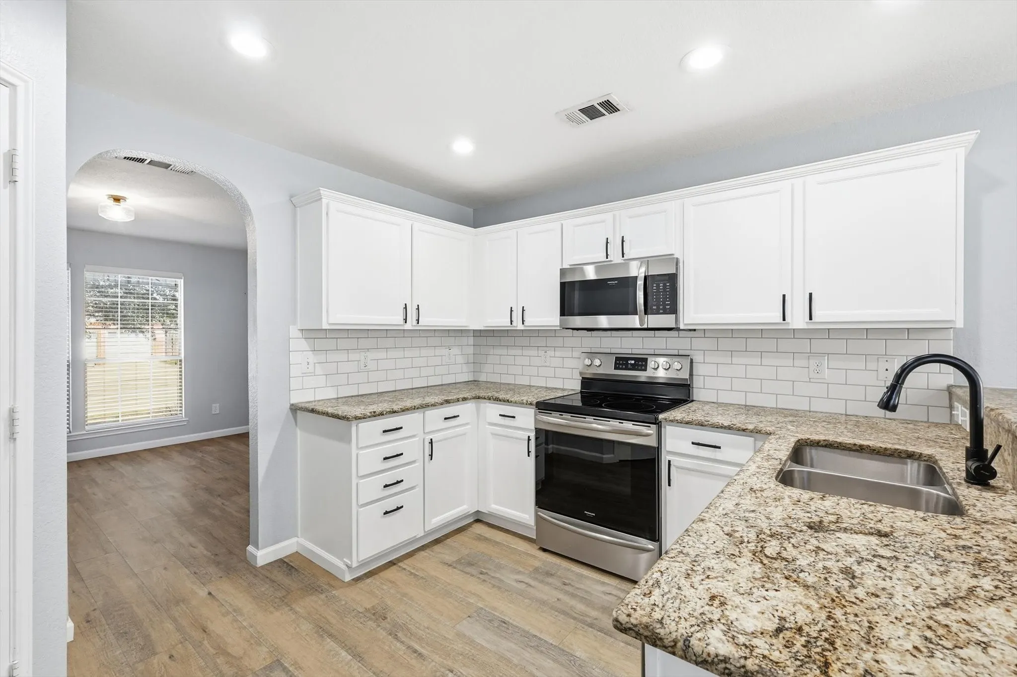 Kitchen with arched walkways, white cabinetry, backsplash, light stone countertops, and recessed lighting