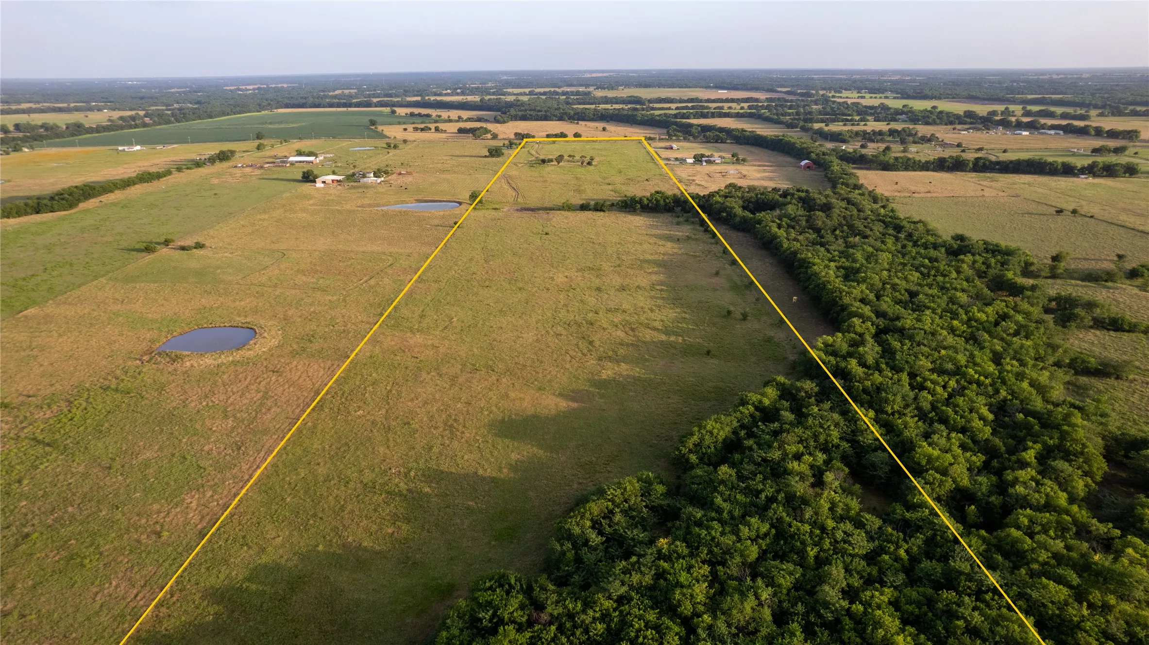 Expansive acreage featuring a natural pond, established tree lines, open pastures, and distant structures
