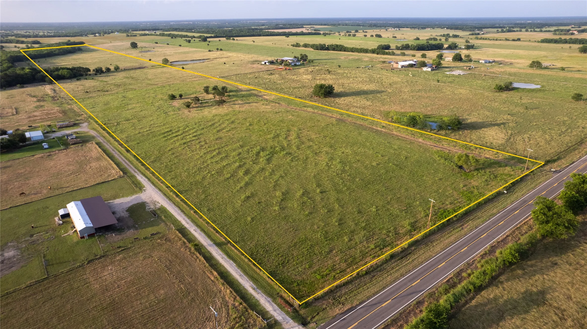 Expansive green acreage featuring a large field, a pond, and direct road frontage