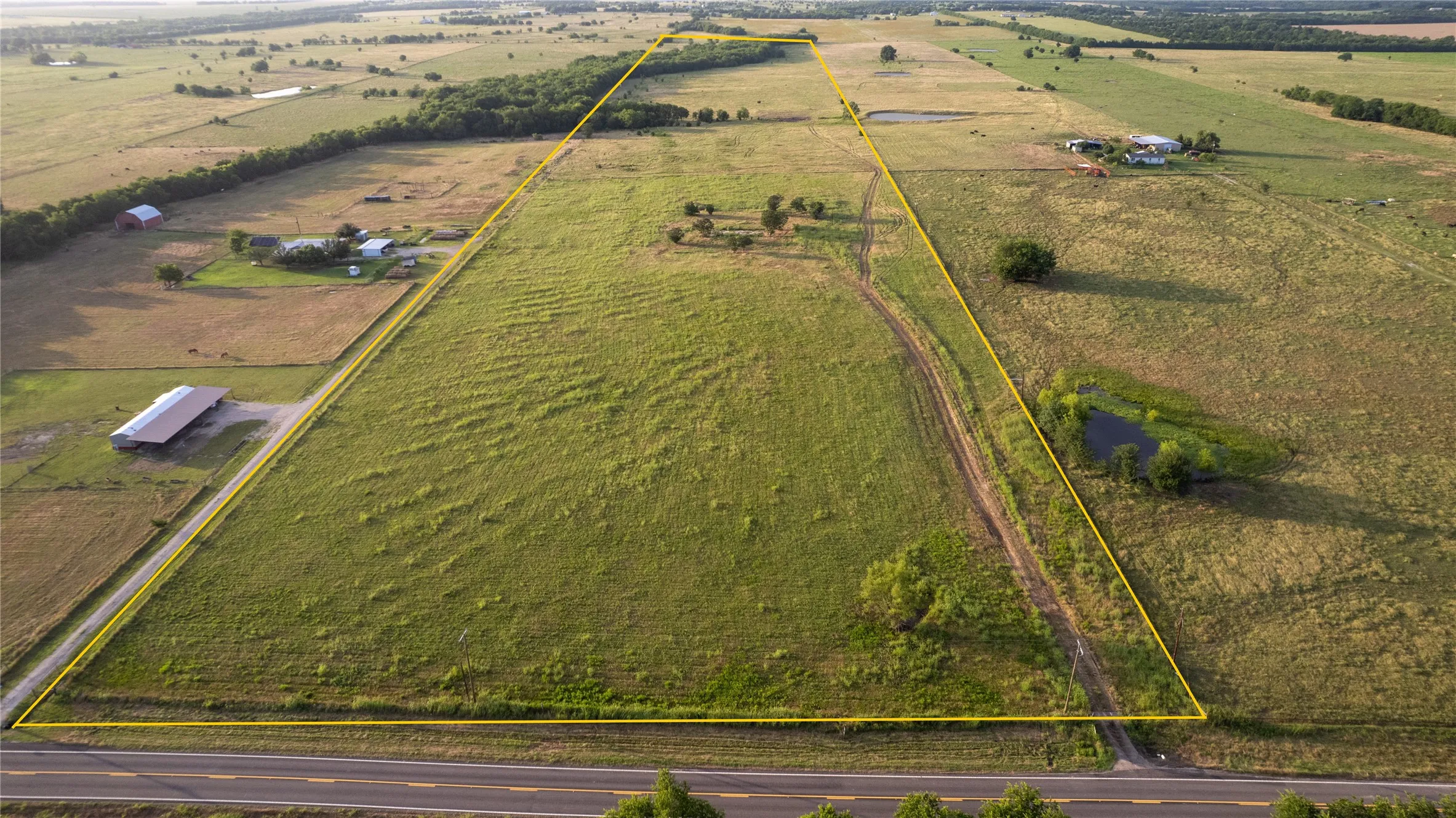 Expansive agricultural land featuring a natural pond, scattered mature trees, and direct road frontage