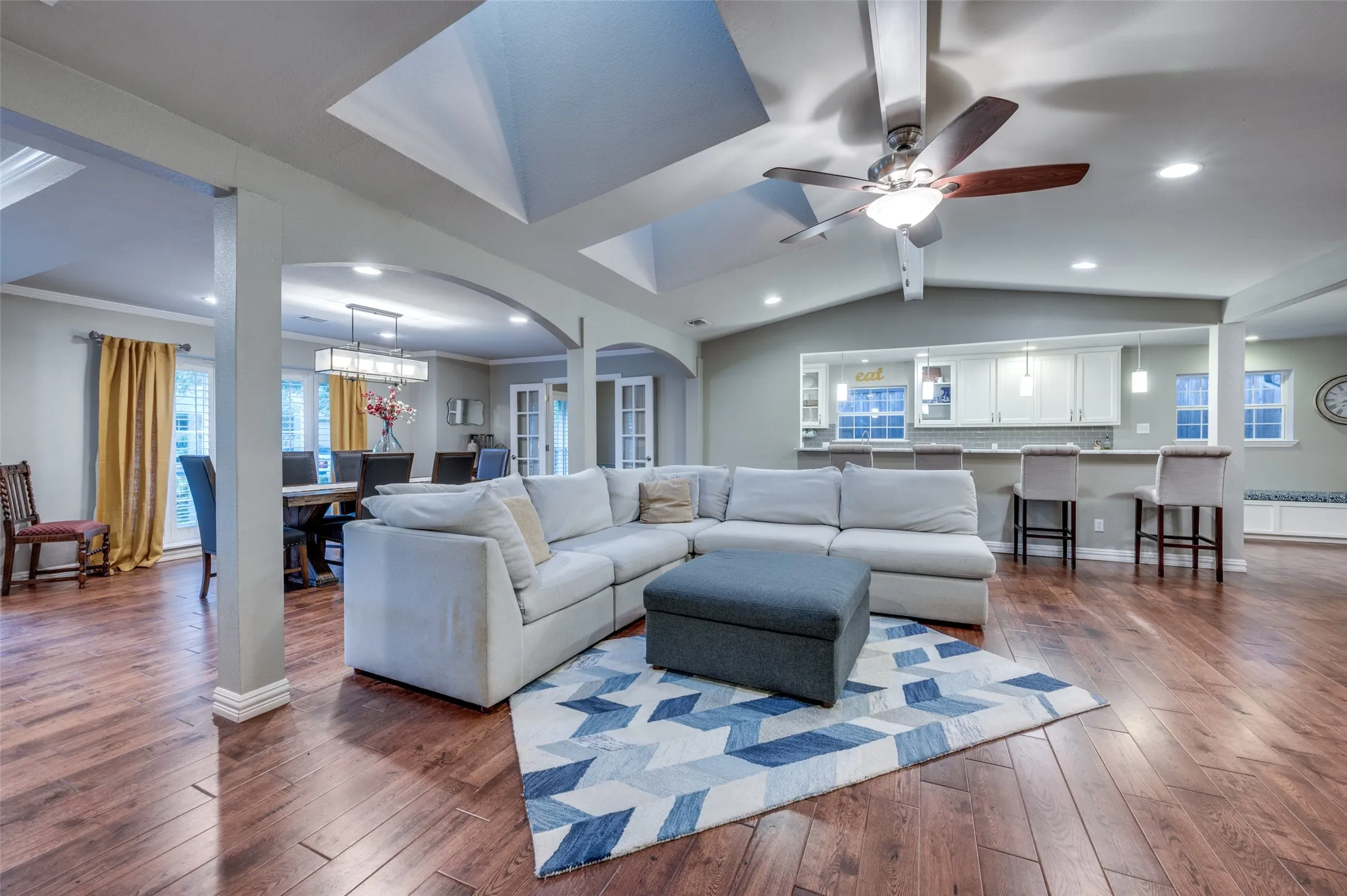 Living room with dark wood-style flooring, arched walkways, ceiling fan, recessed lighting, and lofted ceiling