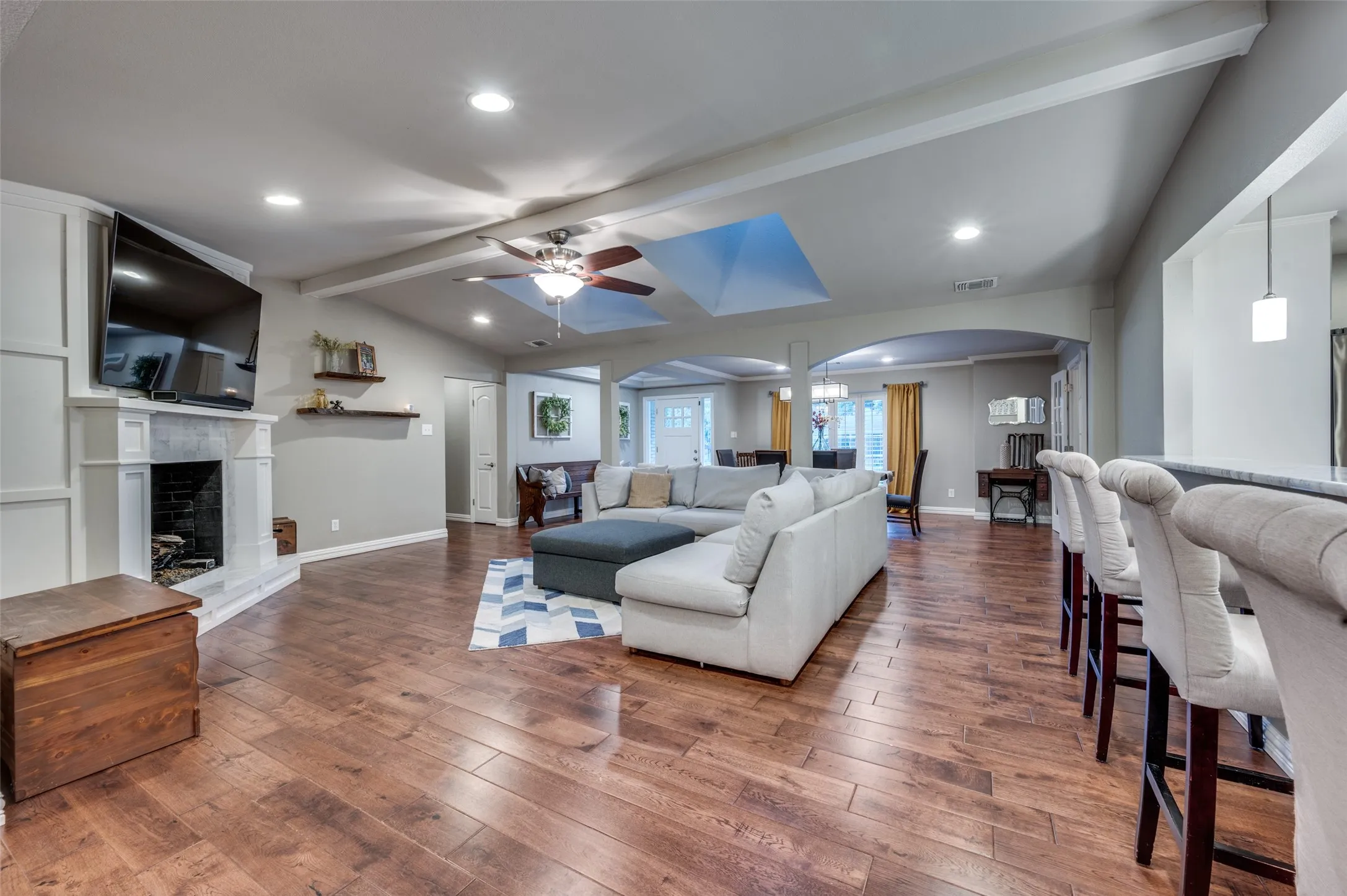 Living area with arched walkways, a ceiling fan, wood-type flooring, a fireplace with raised hearth, and recessed lighting