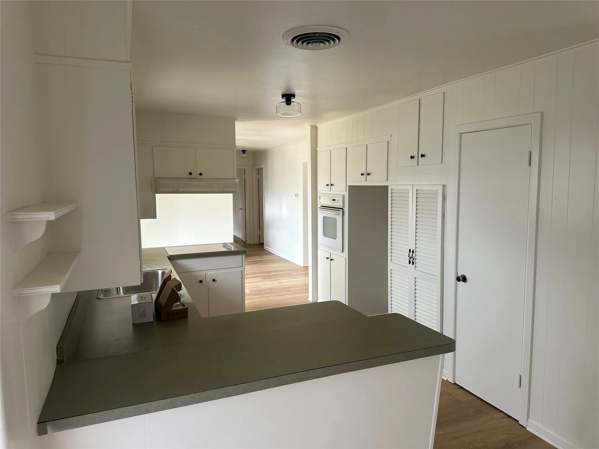 Kitchen with a peninsula, white oven, under cabinet range hood, and white cabinetry