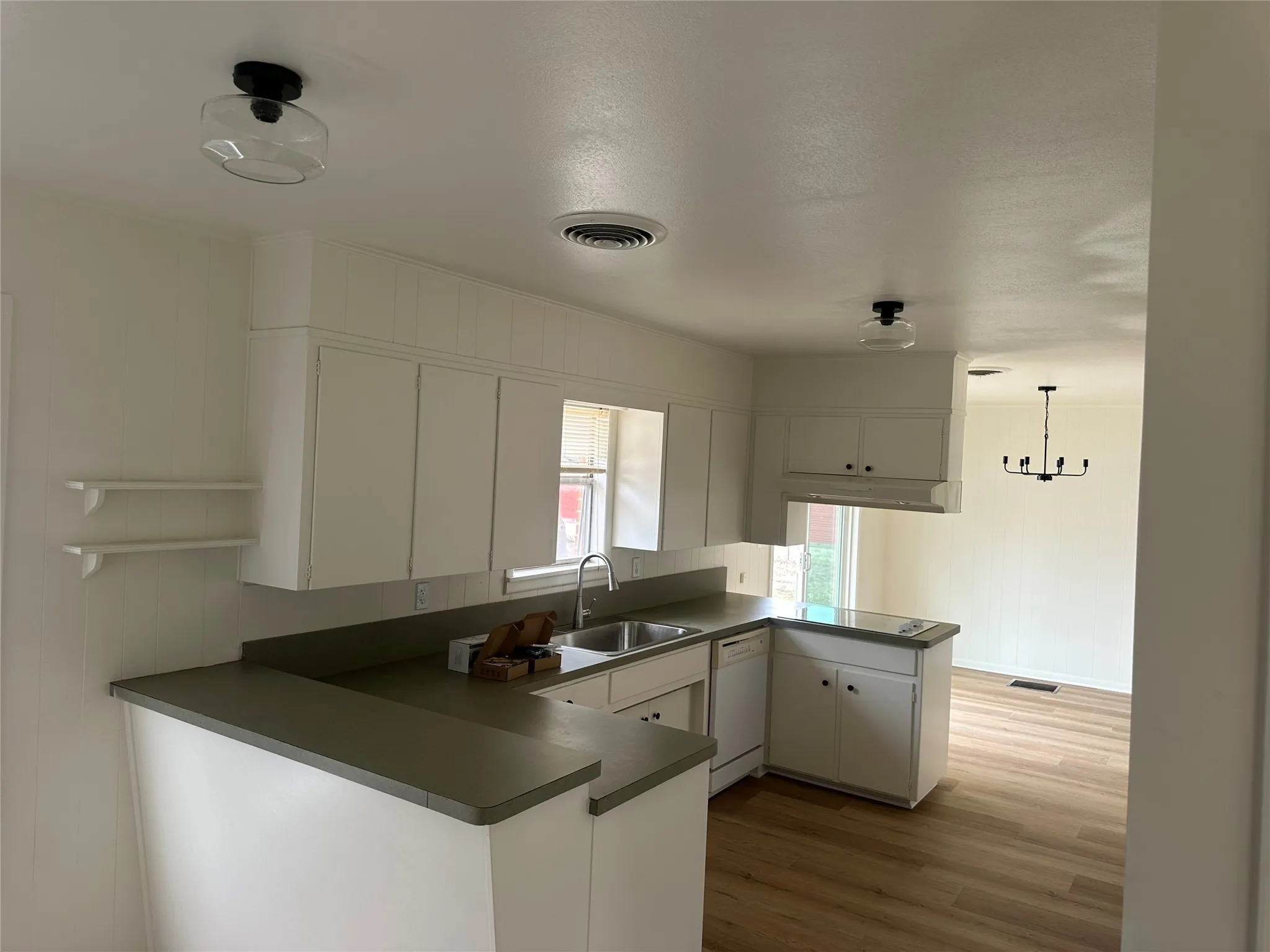 Kitchen featuring a peninsula, dark countertops, dishwasher, and white cabinets