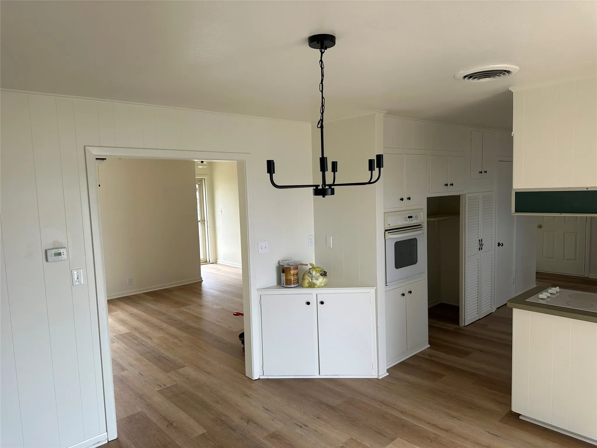 Kitchen featuring white oven, a chandelier, light wood-style flooring, white cabinetry, and decorative light fixtures