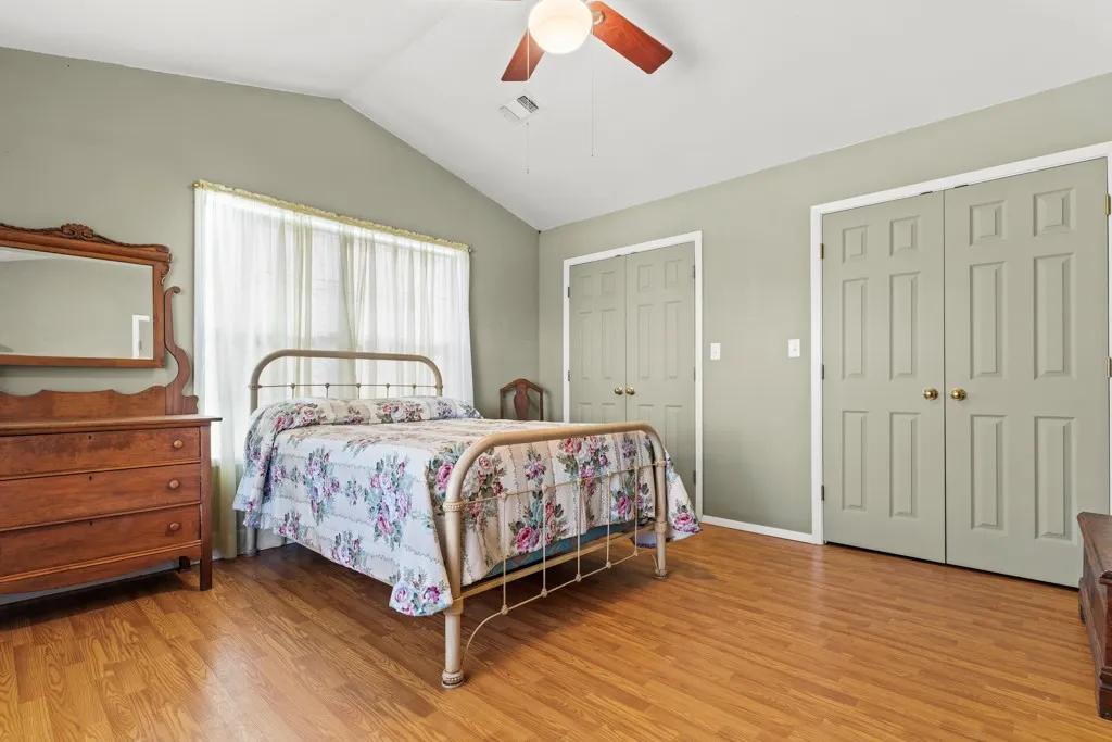 Bedroom featuring two closets, lofted ceiling, light wood-style flooring, and ceiling fan