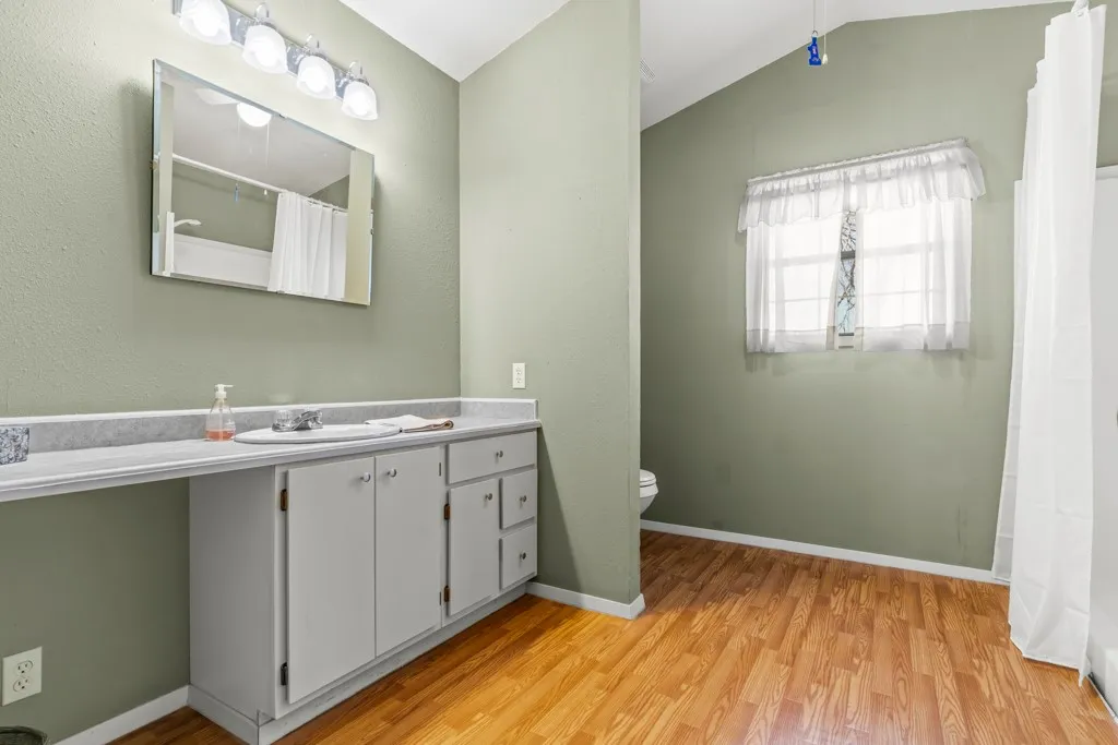 Full bathroom featuring vanity, vaulted ceiling, light wood-style floors, and curtained shower