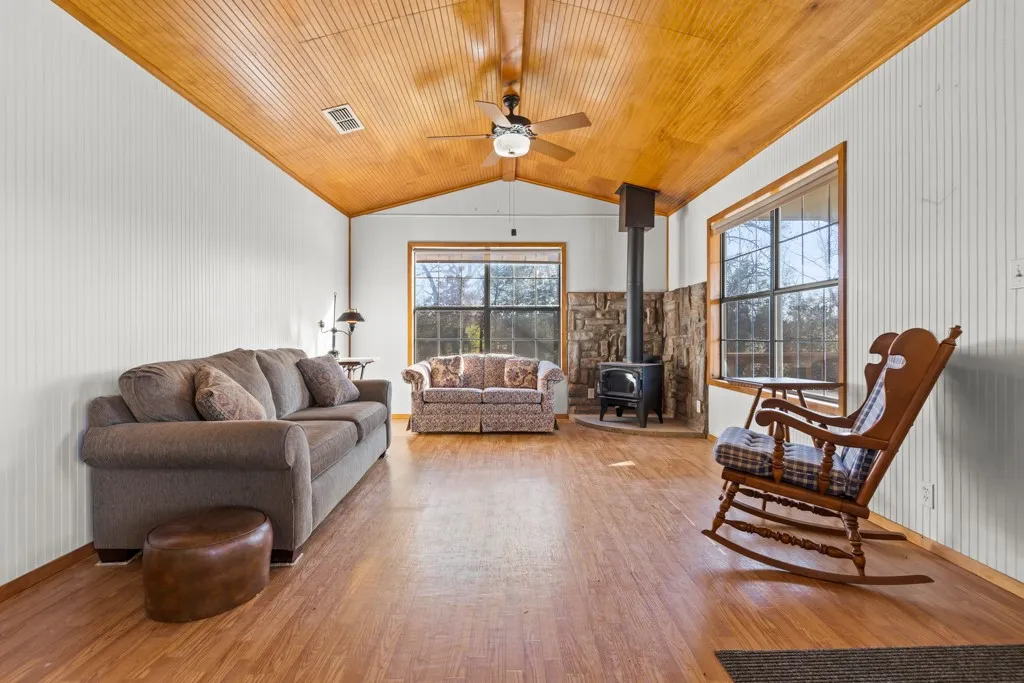 Living room featuring a wood stove, vaulted ceiling, light wood-style flooring, ceiling fan, and wood ceiling