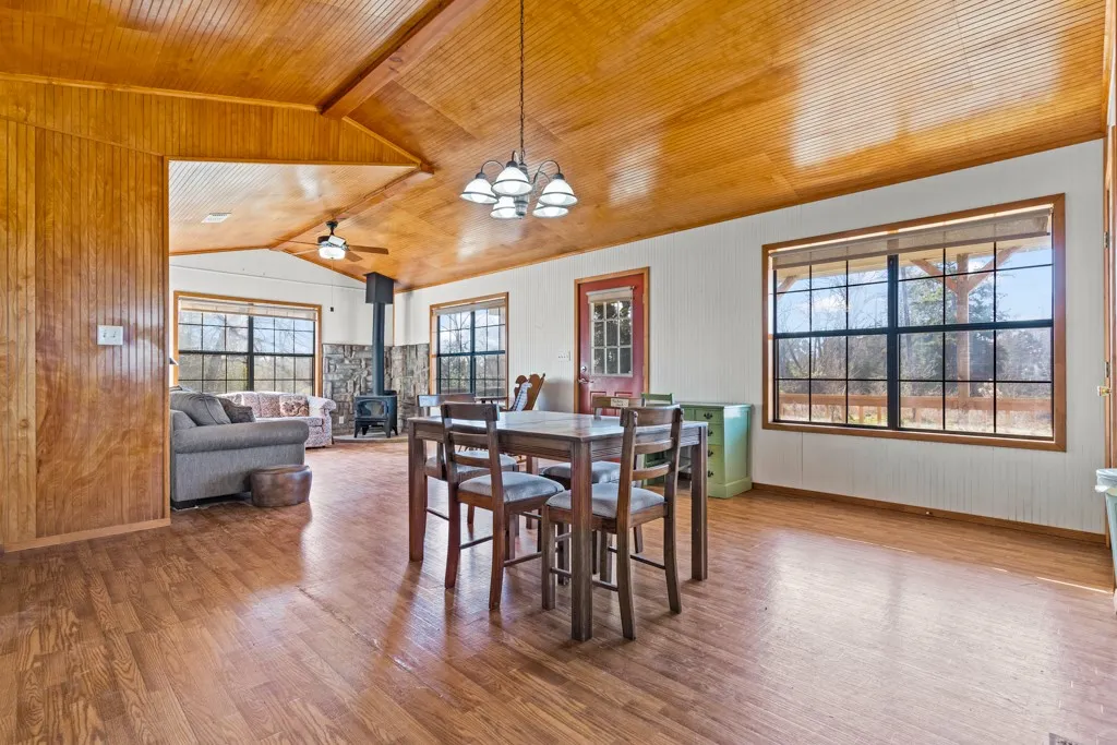 Dining room with a wood stove, light wood-style floors, wood walls, wooden ceiling, and vaulted ceiling