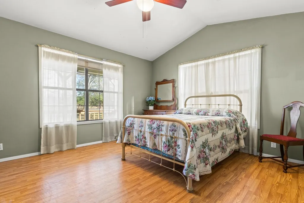Bedroom with vaulted ceiling, light wood-style floors, multiple windows, and ceiling fan