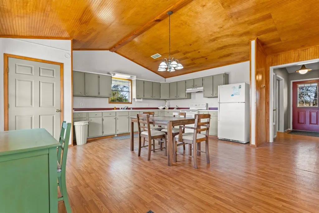 Kitchen featuring green cabinetry, hanging light fixtures, white appliances, a chandelier, and light wood-style flooring