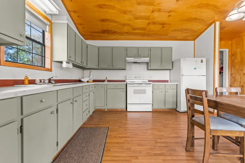 Kitchen with white appliances, light countertops, light wood-type flooring, under cabinet range hood, and wooden ceiling