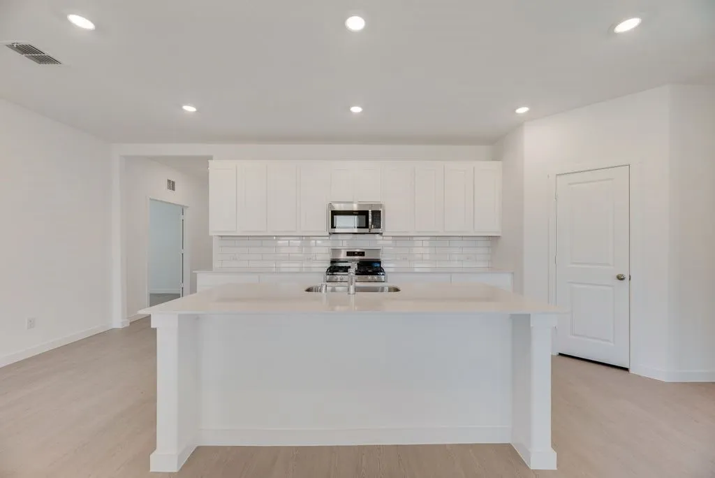 Kitchen with backsplash, light countertops, light wood-style floors, appliances with stainless steel finishes, and white cabinets