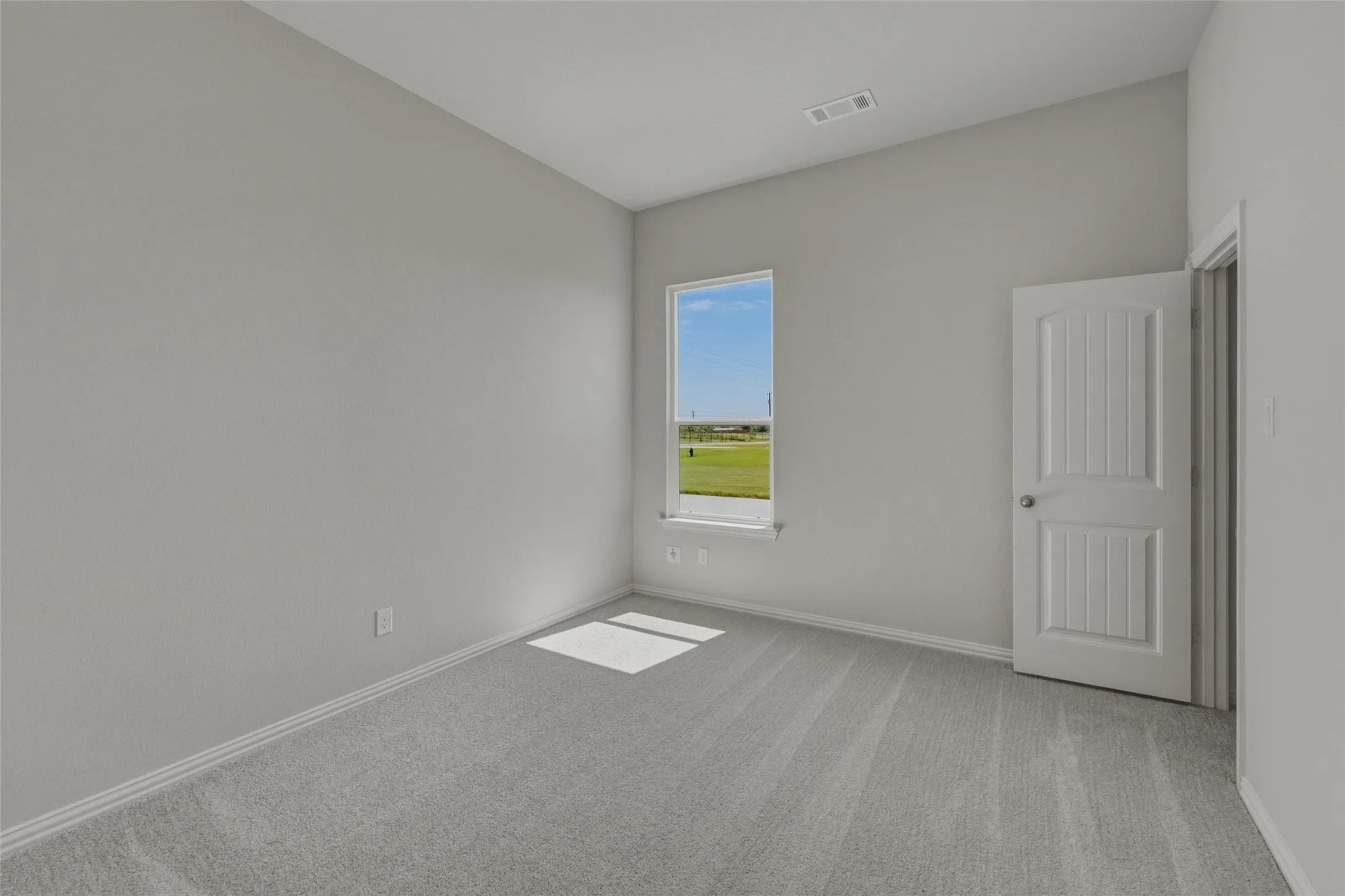 Bright interior room featuring a large window, light gray carpet, and a white paneled door